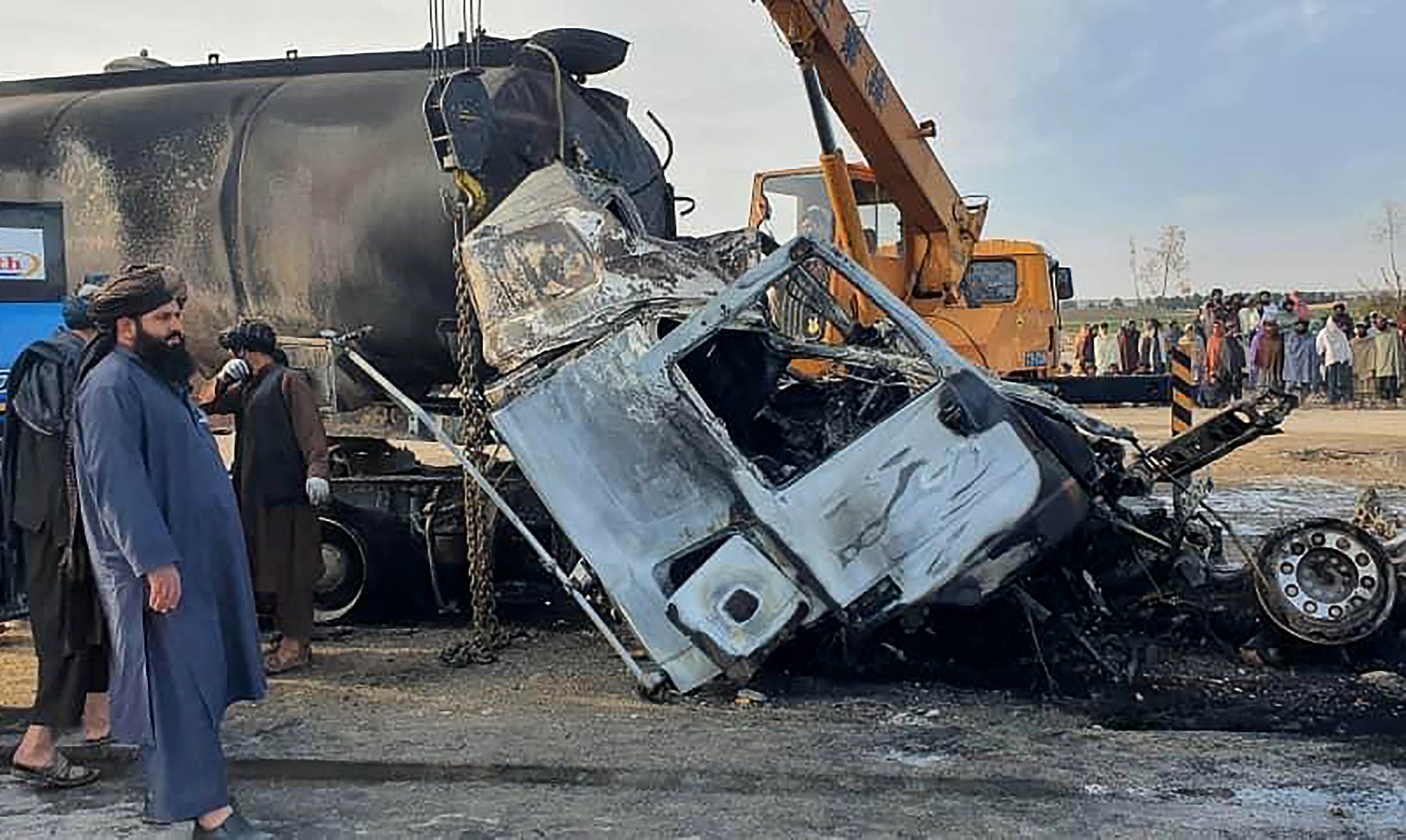 Security personnel and volunteers standing near the wreckage of a burned passenger bus and oil tanker on the Herat-Kandahar highway in the Grishk district of Helmand province