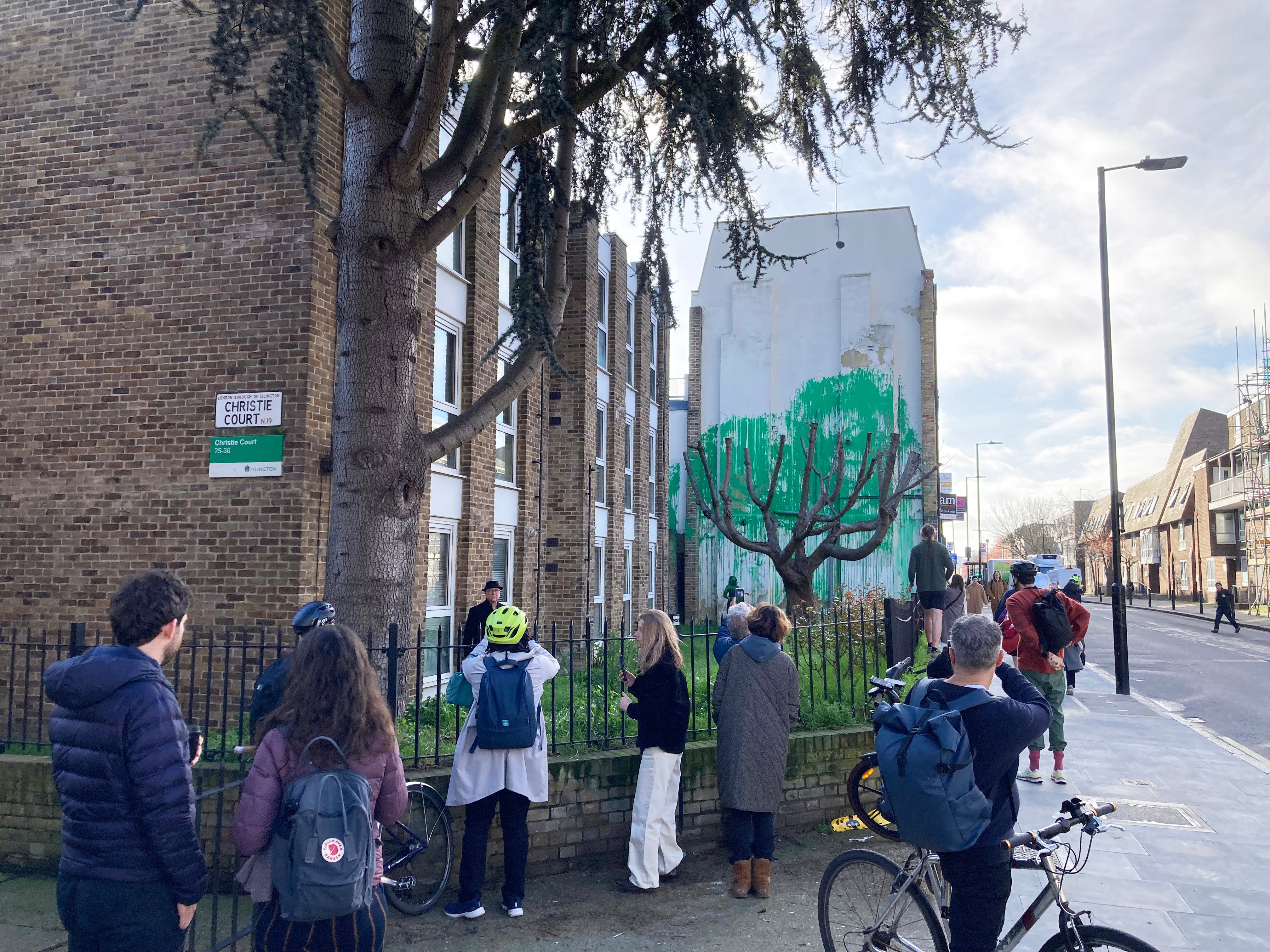 Members of the public look at a new piece of art work, which has appeared on the side of a building on Hornsey Road