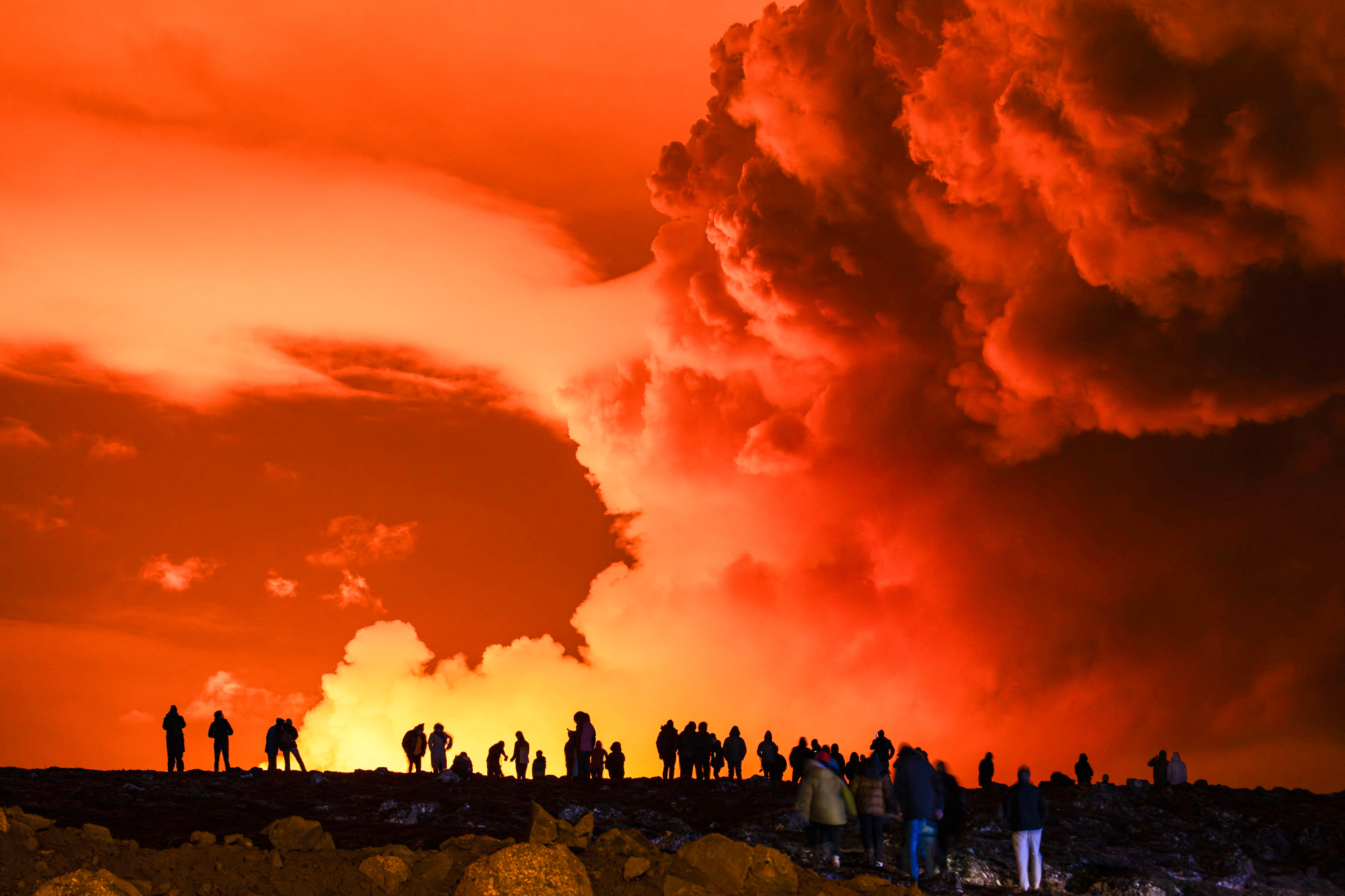 People gather to watch as molten lava flows out from a fissure on the Reykjanes peninsula north of the evacuated town of Grindavik, western Iceland on 16 March