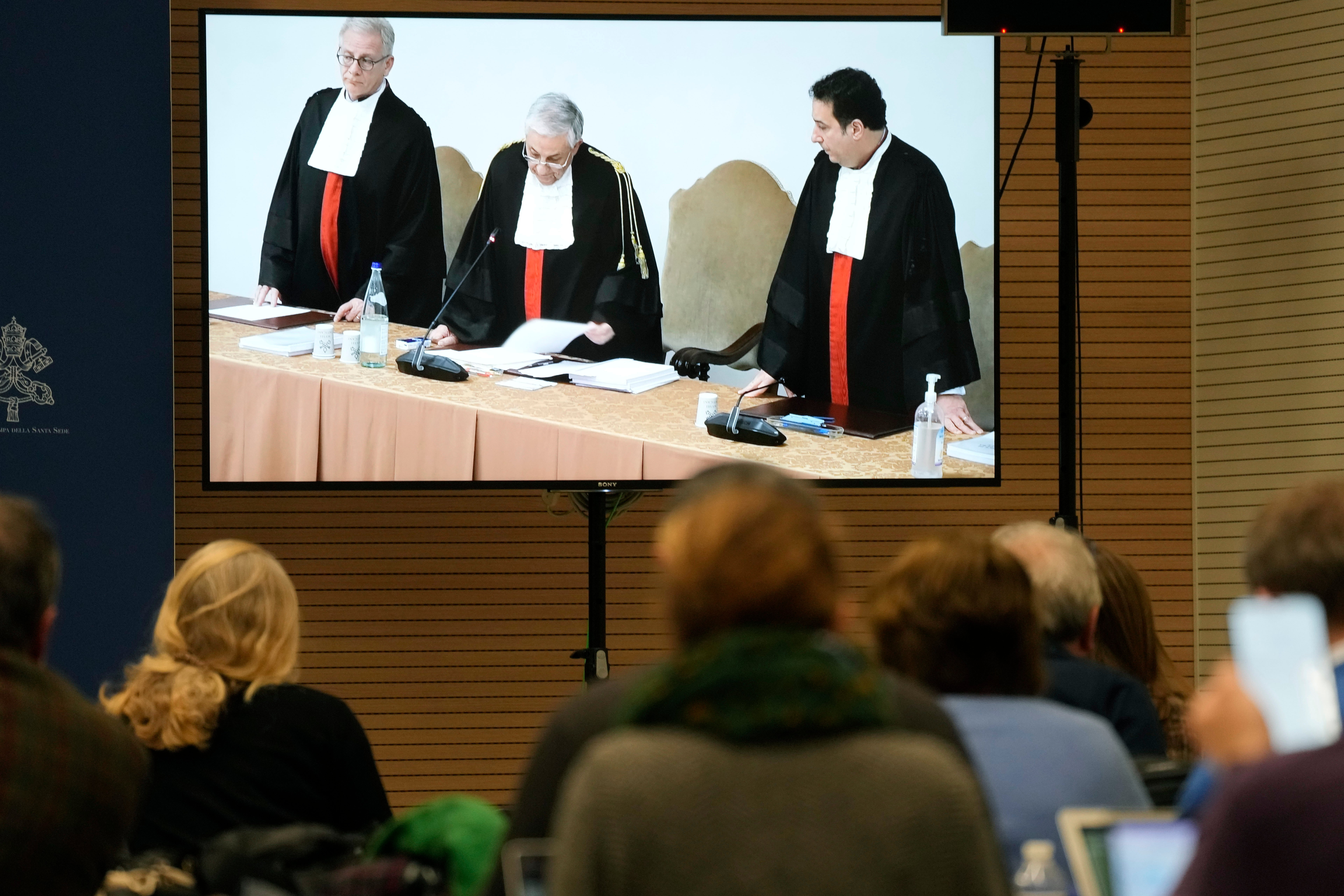 Reporters watch a screen in the Vatican press room showing Vatican tribunal president Giuseppe Pignatone reading the verdict of a trial against Cardinal Angelo Becciu and nine other defendants