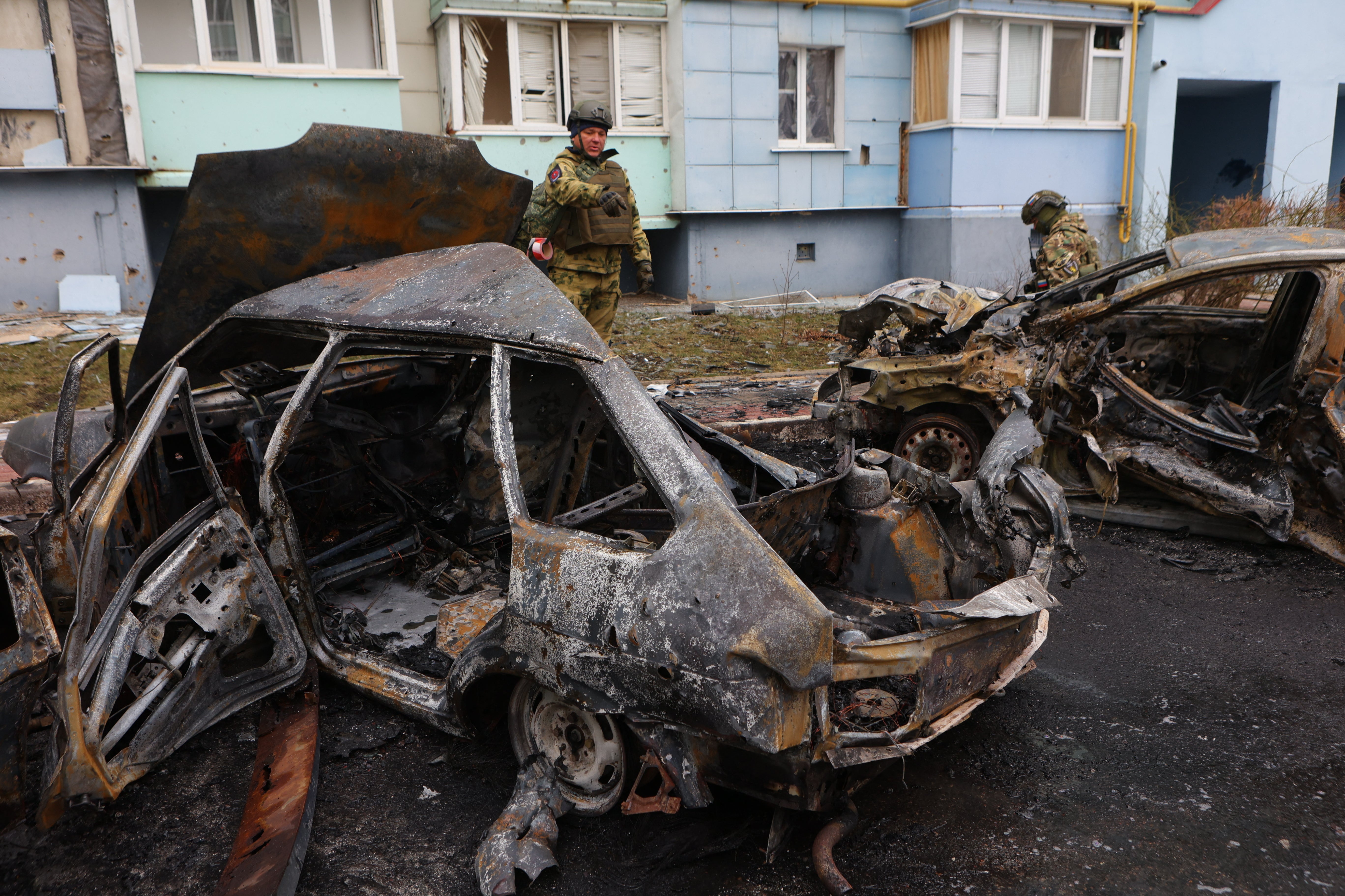 Self-defence unit volunteers stand by burned-out cars in a residential area of the city of Belgorod following fresh aerial attacks on March 22