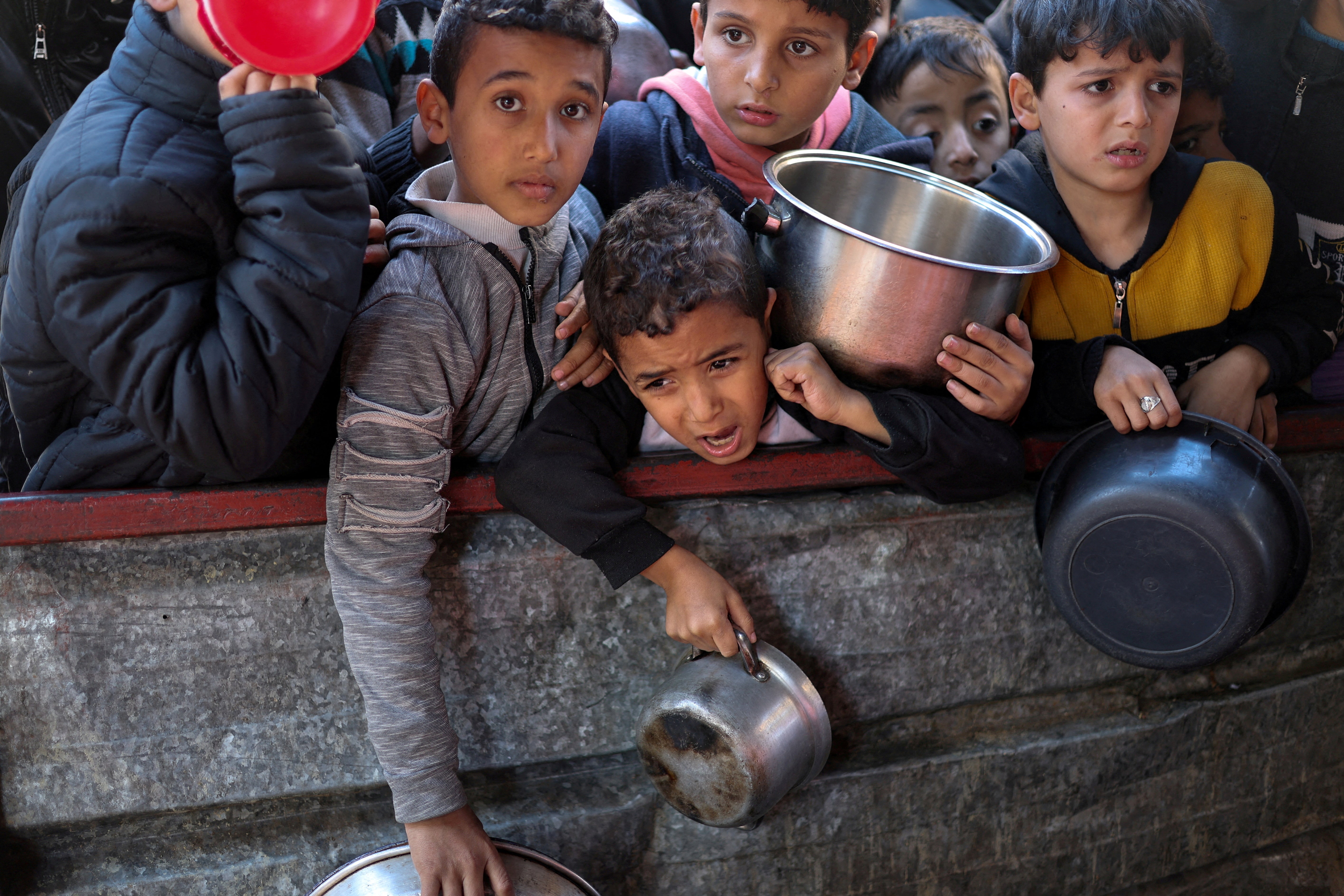 Children in Rafah wait to receive food provided by a charity kitchen