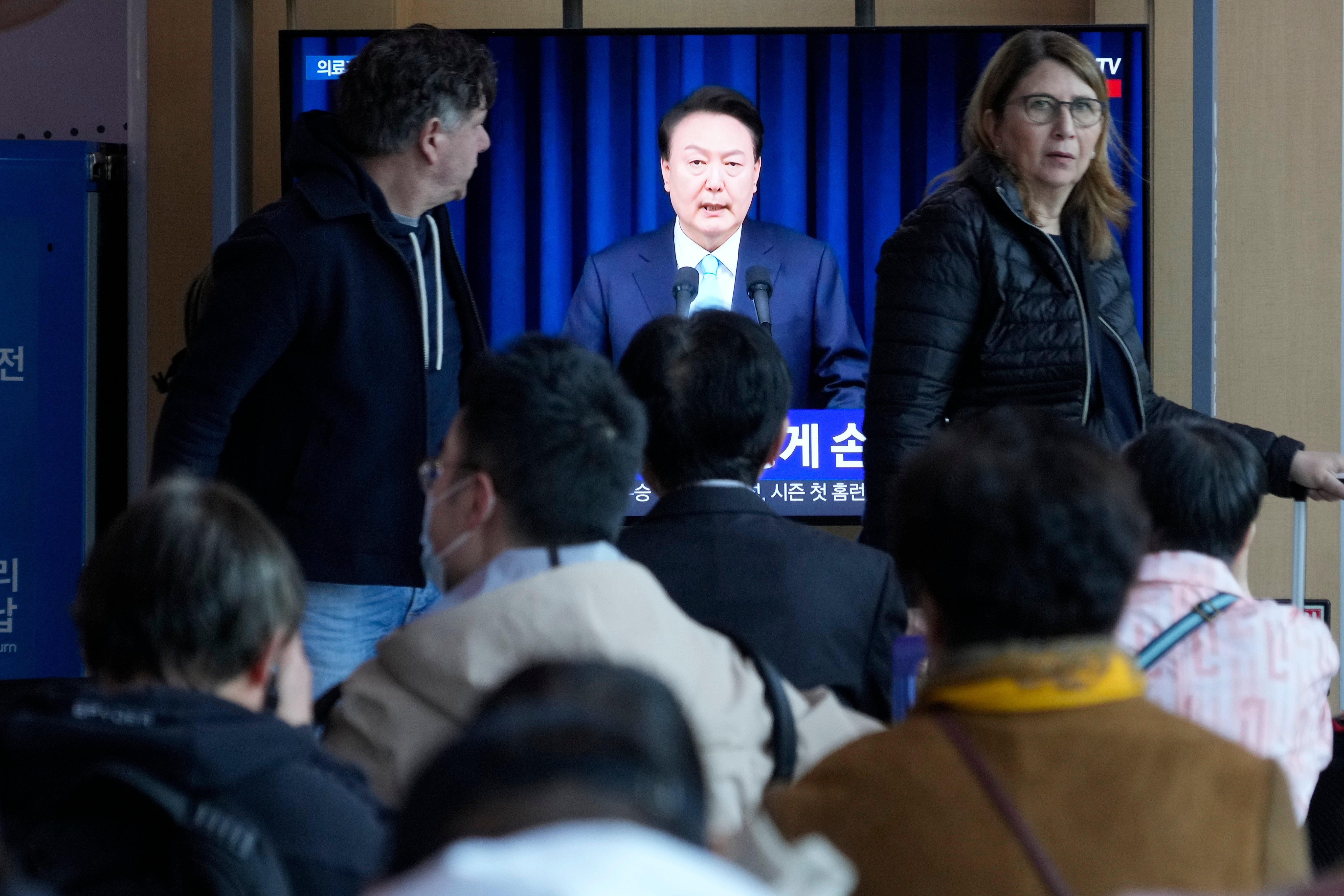 People watch a TV screen showing the live broadcast of South Korean President Yoon Suk Yeol’s addressing the nation at the Seoul Railway Station in Seoul