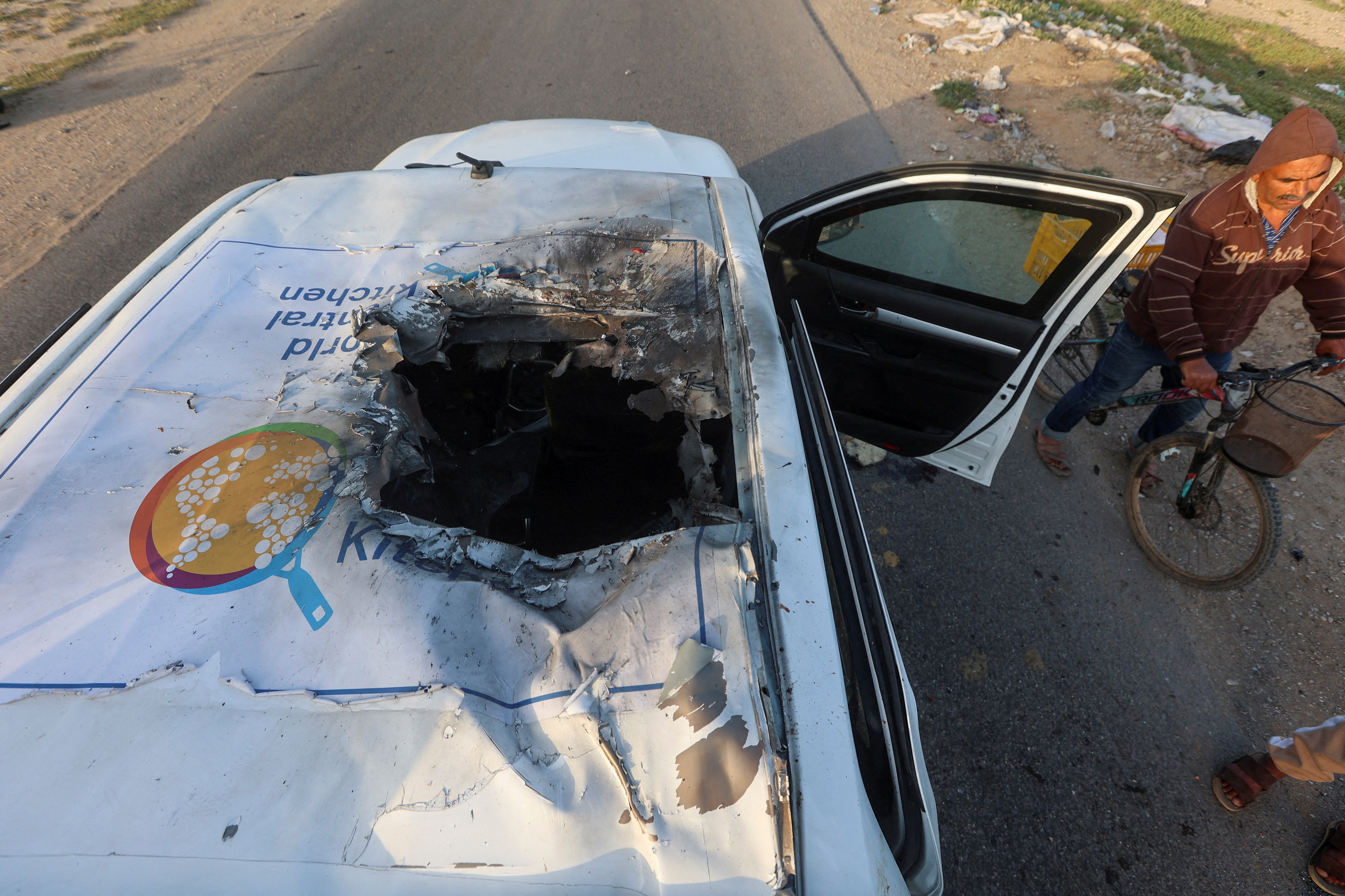 A Palestinian man rides a bicycle past a damaged vehicle where employees from the World Central Kitchen (WCK), including foreigners, were killed in an Israeli airstrike amid the ongoing conflict between Israel and Hamas, in Deir Al-Balah, in central Gaza Strip on 2 April 2024