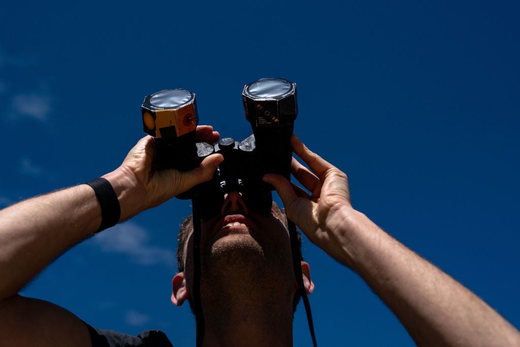 Frederik De Vries who is visiting from Amsterdam, looks up at the sun using binoculars outfitted with solar film, as people gather on the National Mall to view the partial solar eclipse on 8 April, 2024 in Washington, DC