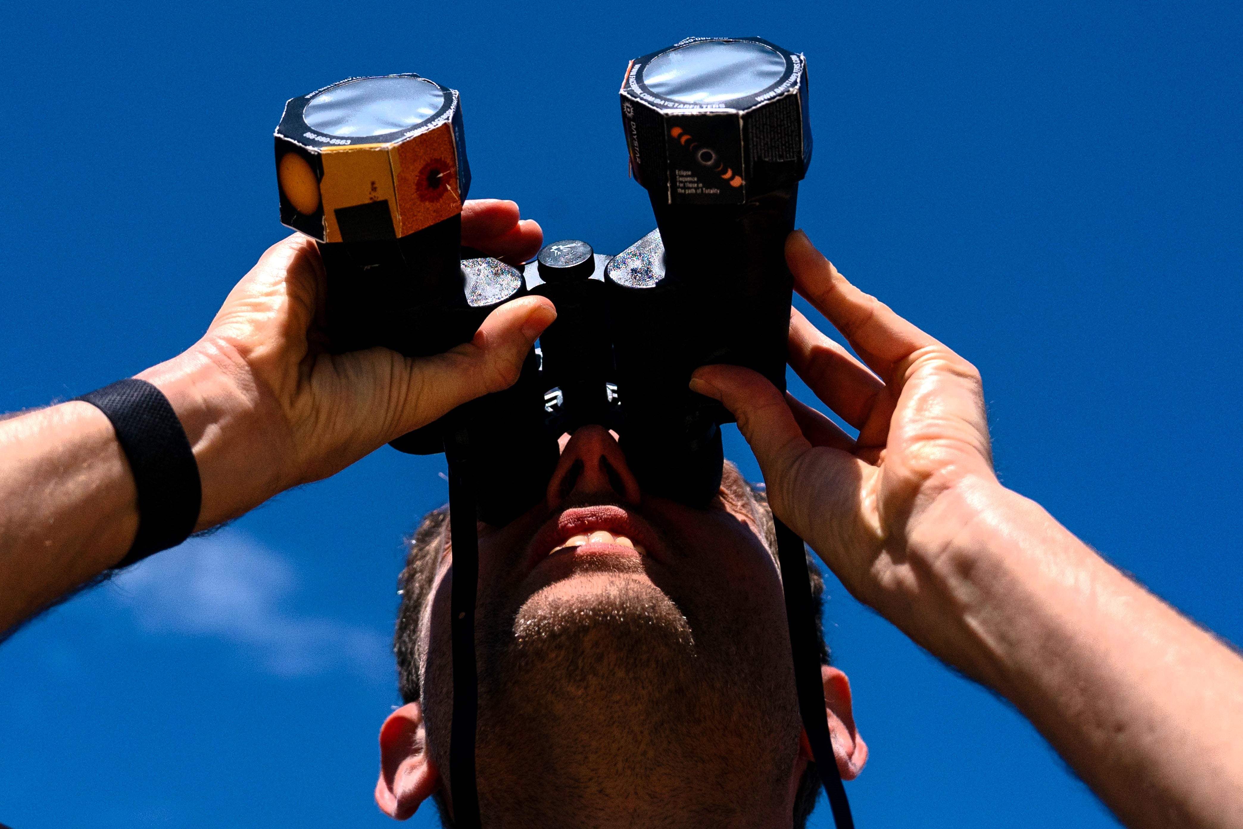 Frederik De Vries looks up at the sun during the solar eclipse using binoculars outfitted with special film in Washington, DC, on 8 April, 2024
