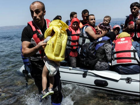 A Syrian migrant helps children get off of an inflatable boat after it arrived on the Greek island of Lesbos after crossing the Aegean sea from Turkey to Greece on August 14, 2015