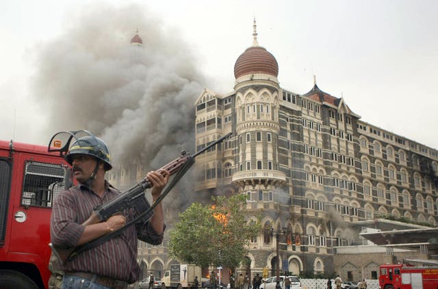 <p>An Indian security official stands alert as smoke and flames billow from the Taj Mahal hotel in Mumbai during terrorist attacks in 2008</p>