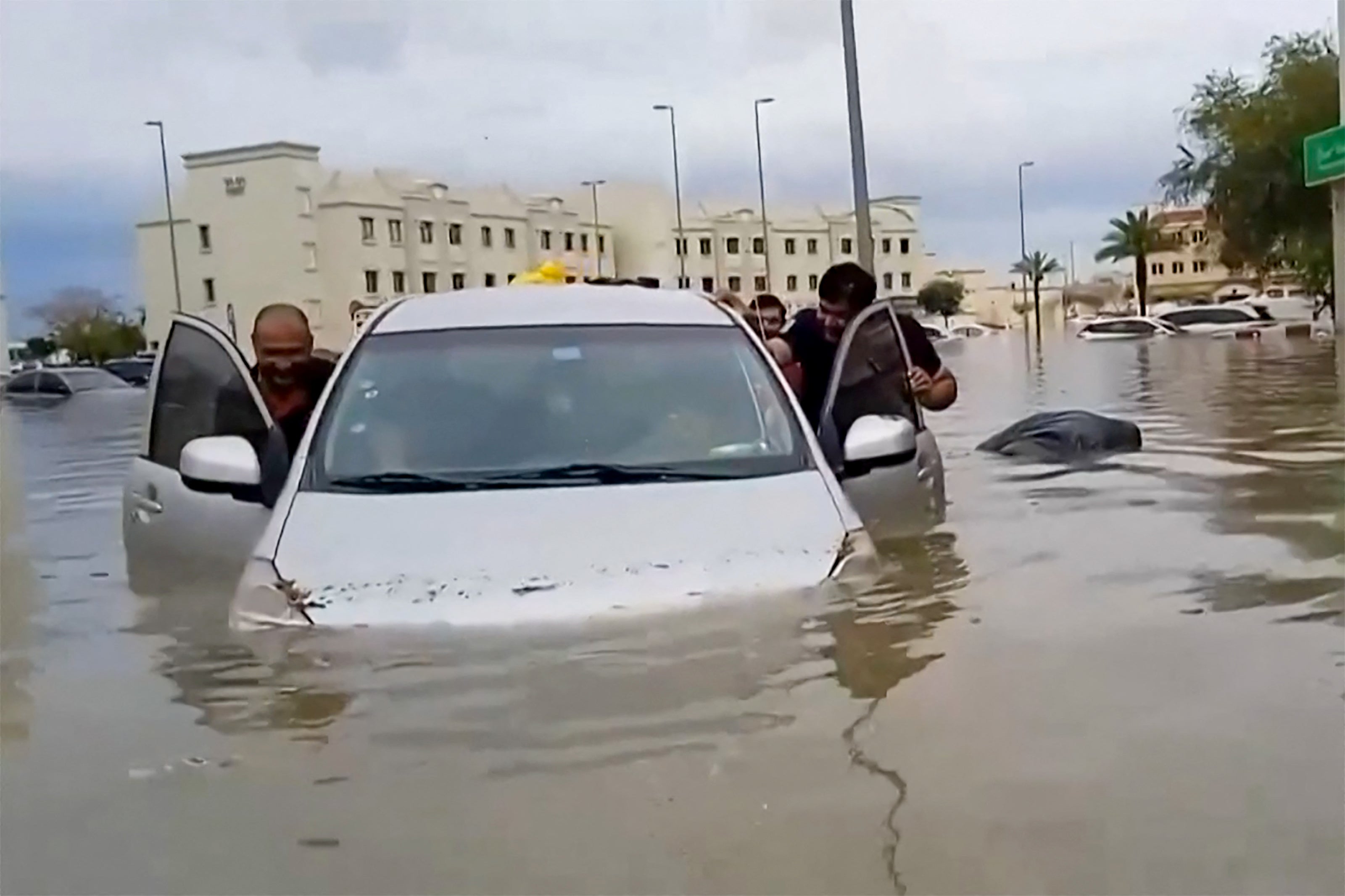 In this video grab from AFPTV, people push a stranded car along a flooded street in Dubai on April 16, 2024