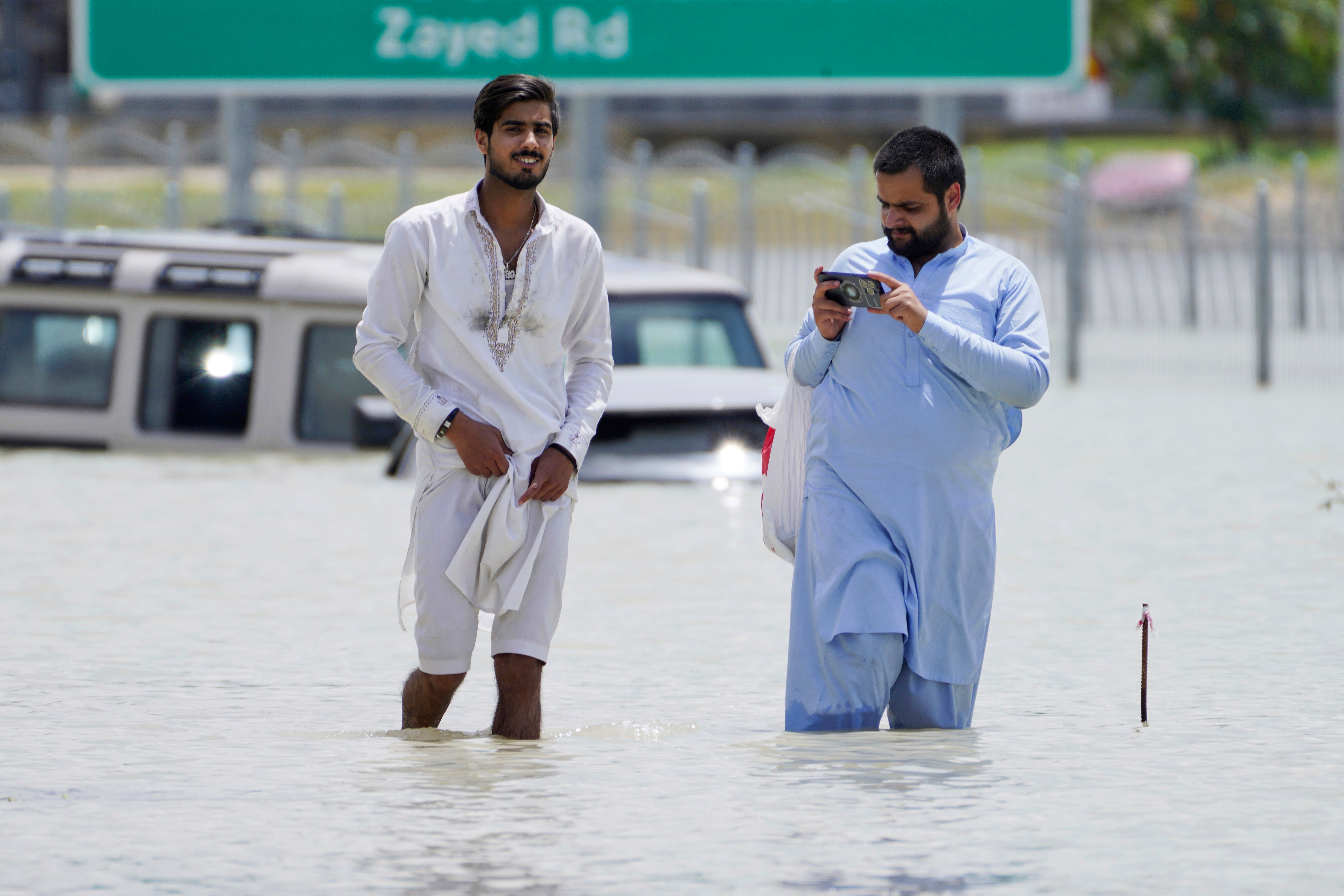 Two men walk through floodwater in Dubai, United Arab Emirates, Wednesday, April 17, 2024