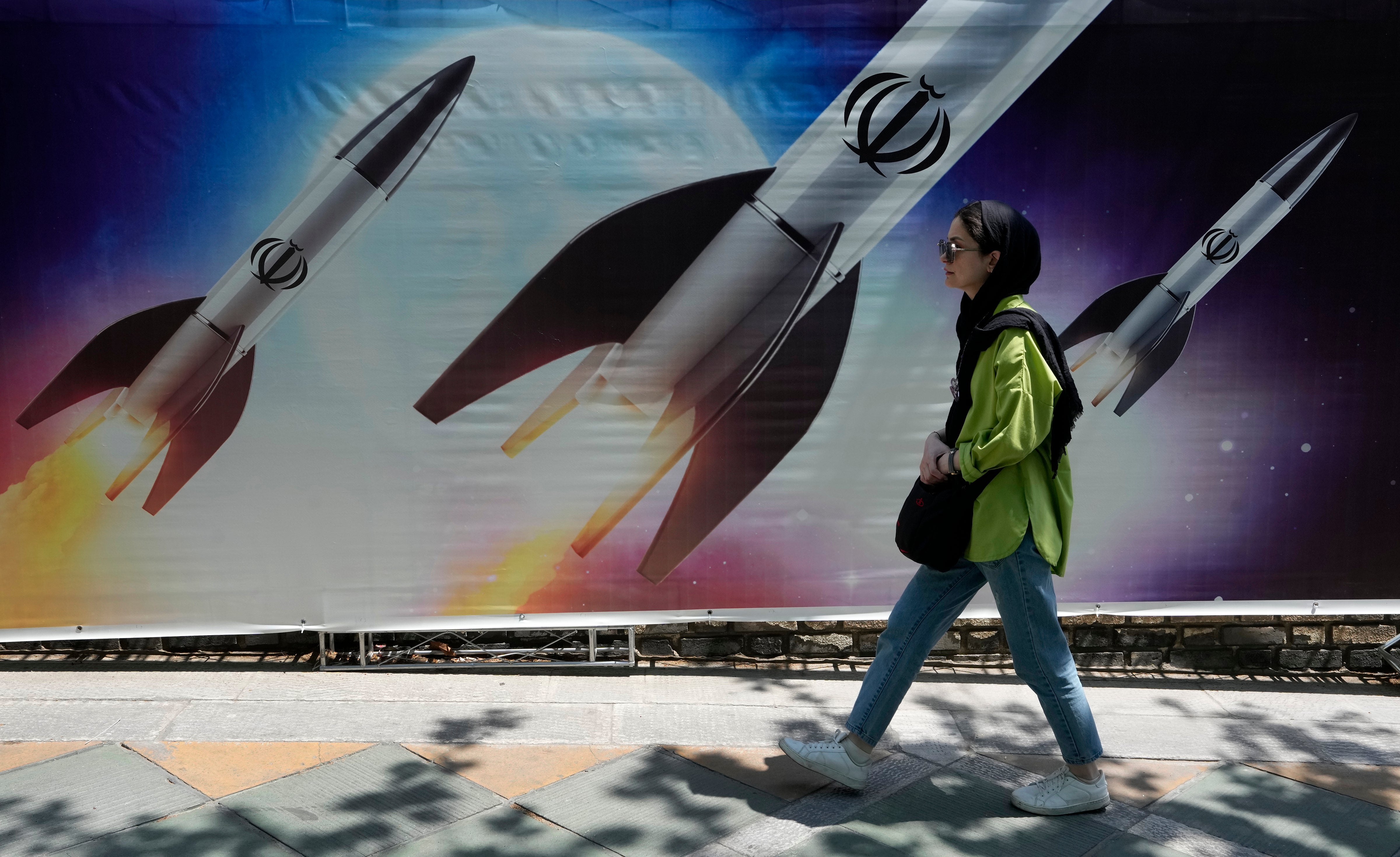 A woman walks past a banner showing missiles being launched, in northern Tehran