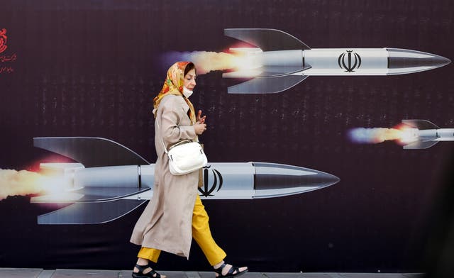 <p>An Iranian woman walks past a huge anti-Israeli banner carrying pictures of missiles, in Tehran, Iran</p>