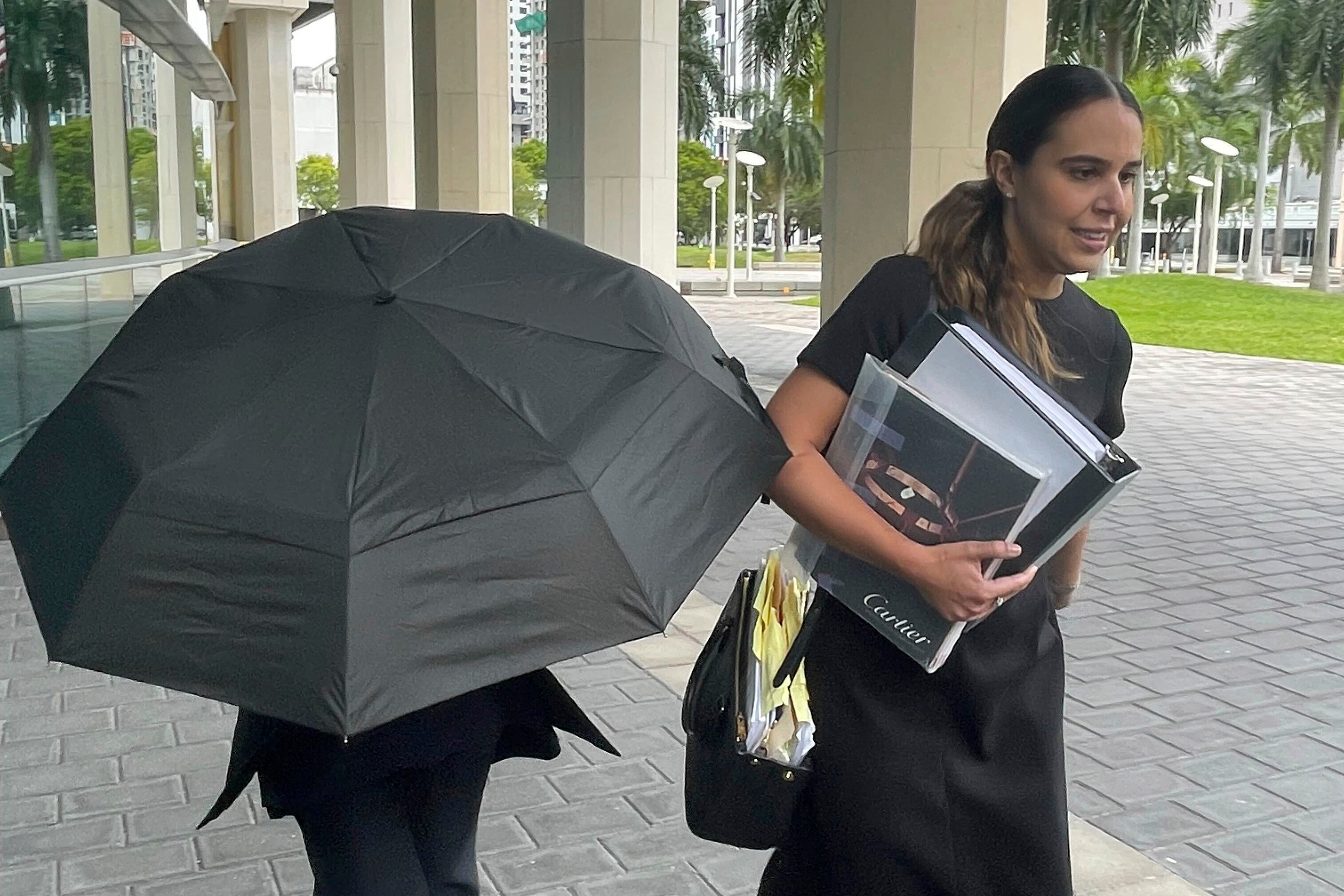 Celebrity handbag designer Nancy Gonzalez hides under an umbrella as she walks with her lawyer Andrea Lopez outside the federal courthouse Monday, April 22, 2024, in Miami.