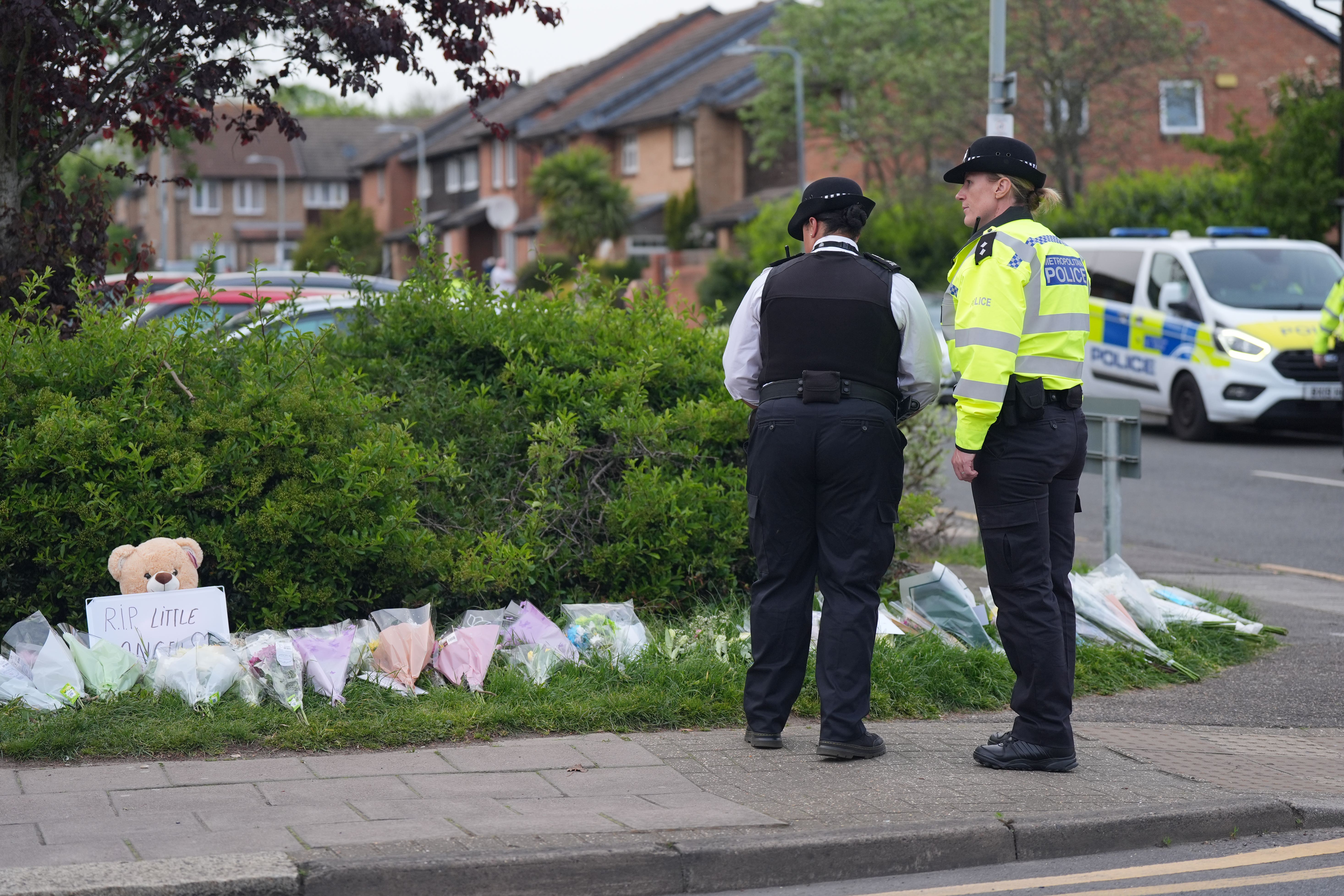 Police officers look at flowers laid at the scene of the incident in Hainault where 14-year-old Daniel Anjorin was killed on Tuesday