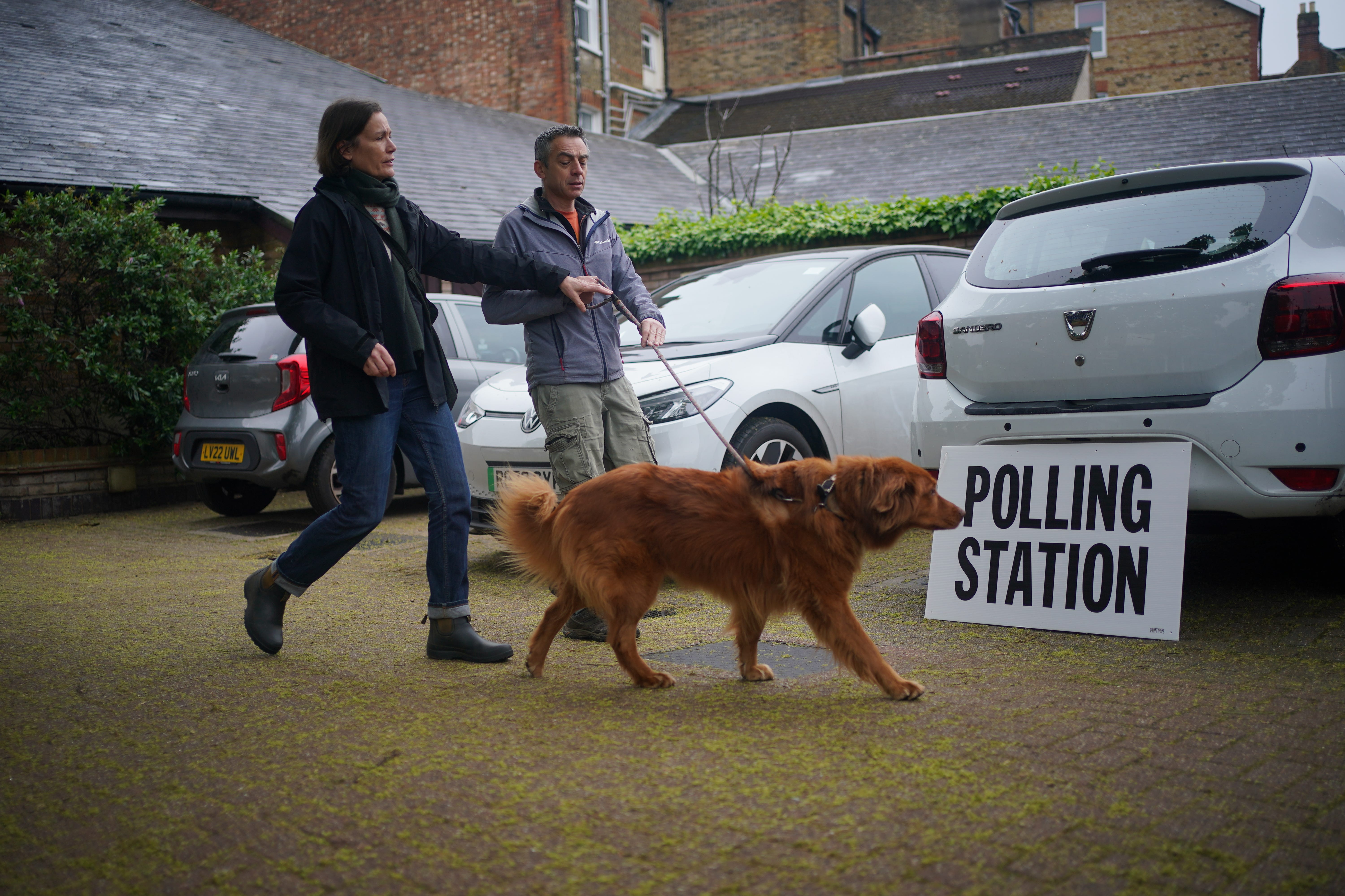 Cinna, an eight-year-old rescue dog from Greece, arrives with its owners at the polling station at St Alban’s Church, south London (PA)