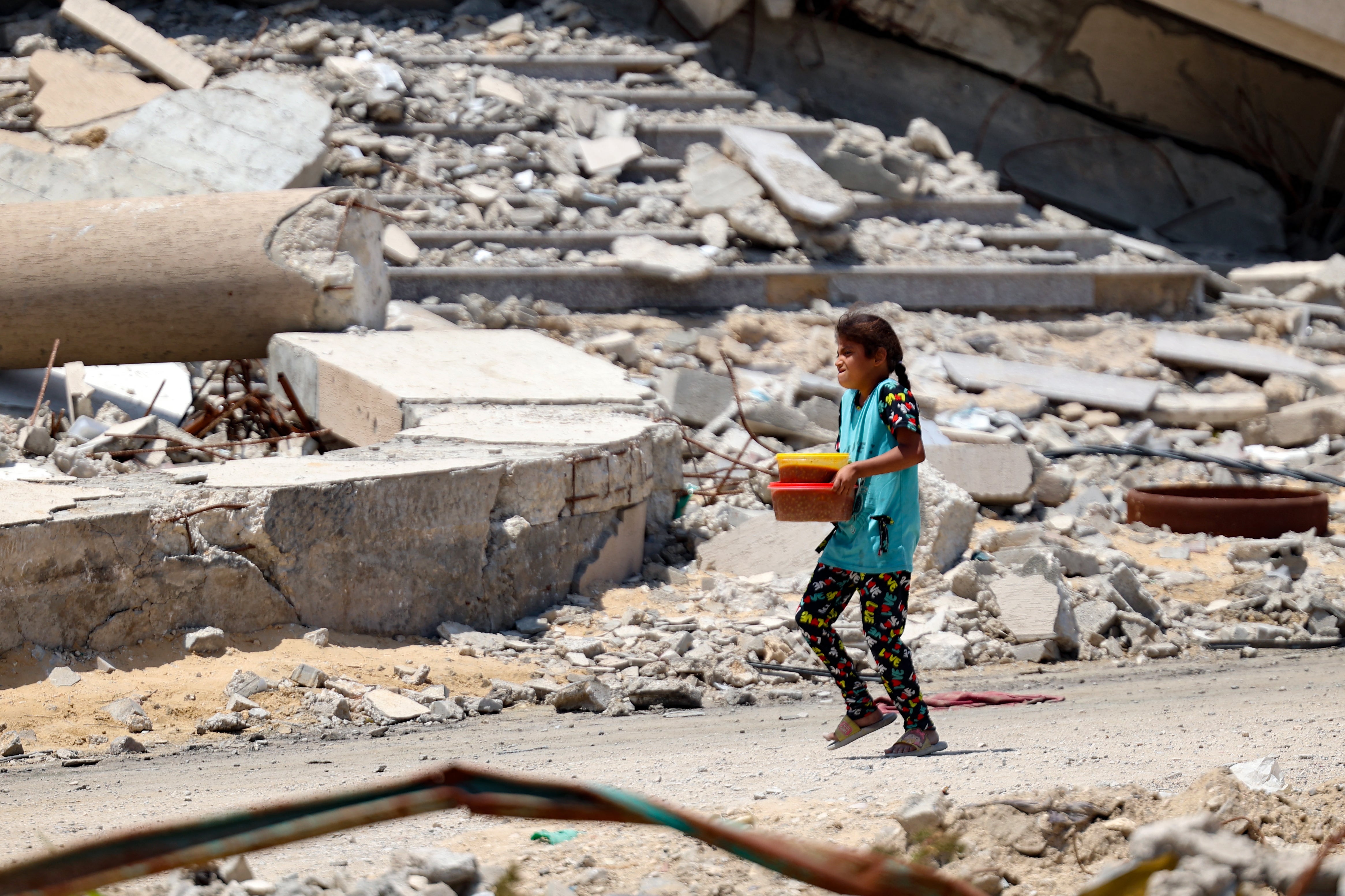 A Palestinian child transporting portions of food walks past a building destroyed by Israeli bombardment in Gaza City in May