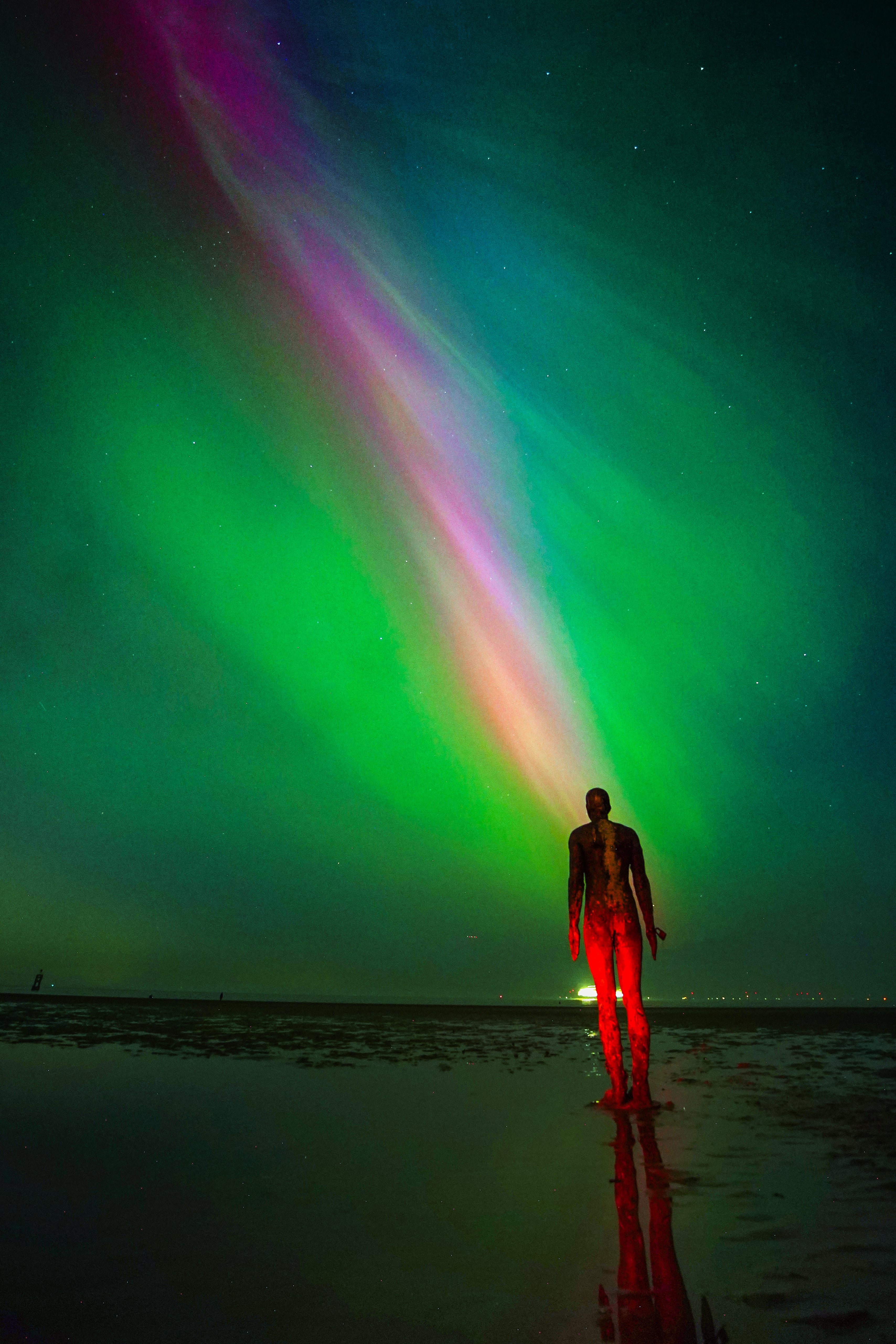 The aurora borealis glow on the horizon at Another Place by Anthony Gormley, Crosby Beach