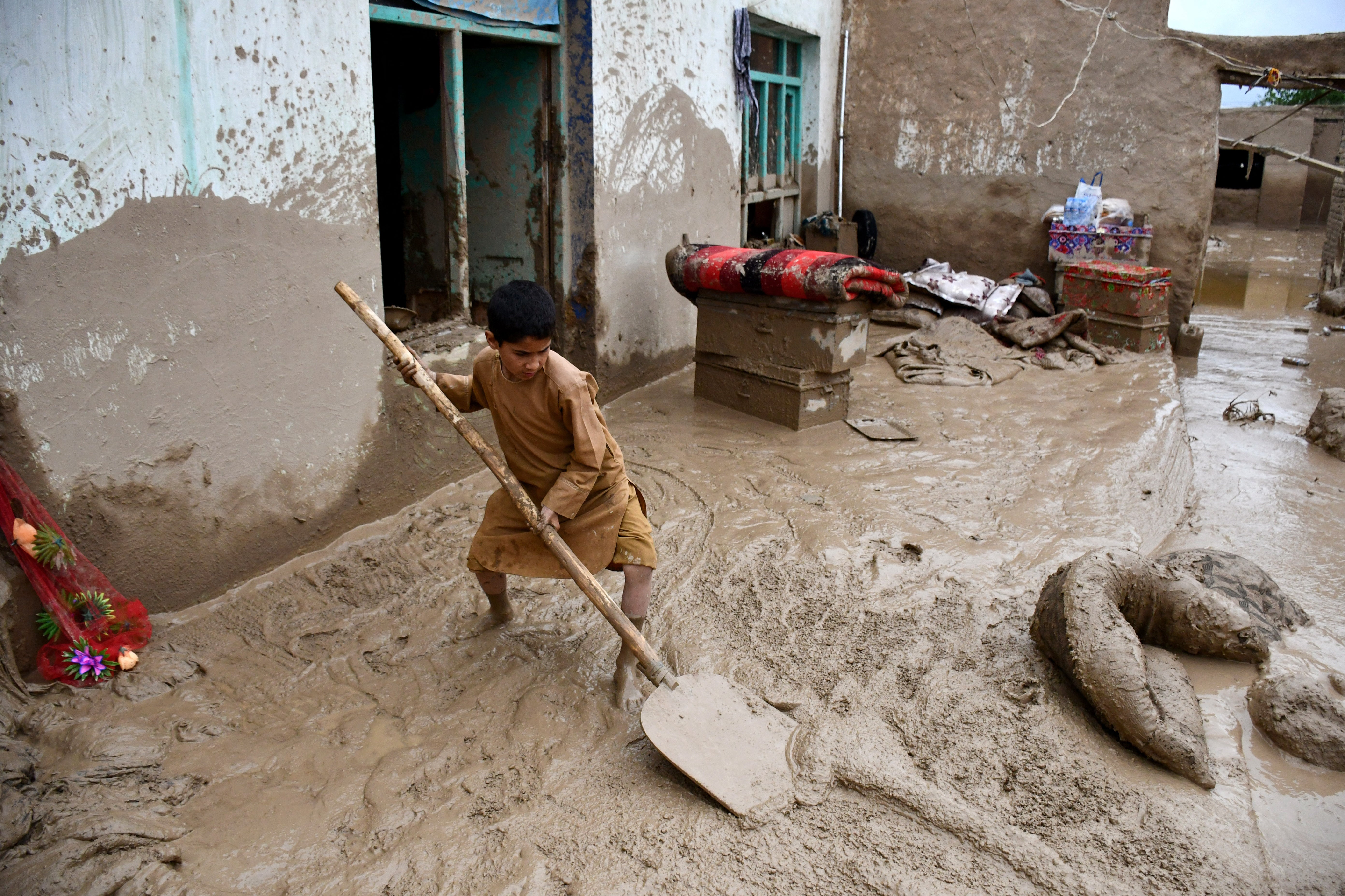 An Afghan boy shovels mud from the courtyard of a house following flash floods after heavy rainfall at a village in Baghlan-e-Markazi district of Baghlan province on 11 May 2024