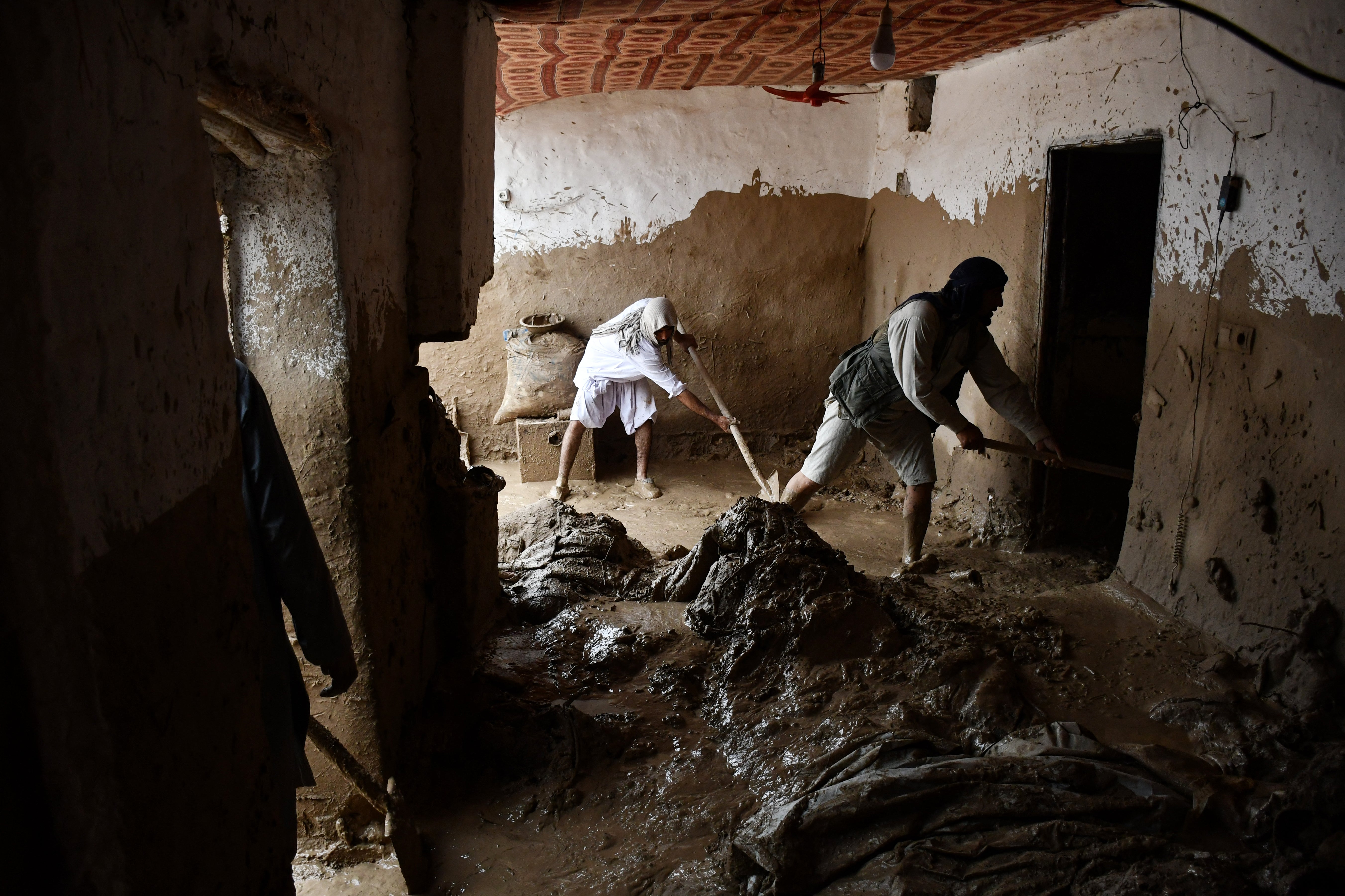 Afghan men shovel mud from a house following flash floods after heavy rainfall at a village in Baghlan-e-Markazi district of Baghlan province on 11 May 2024