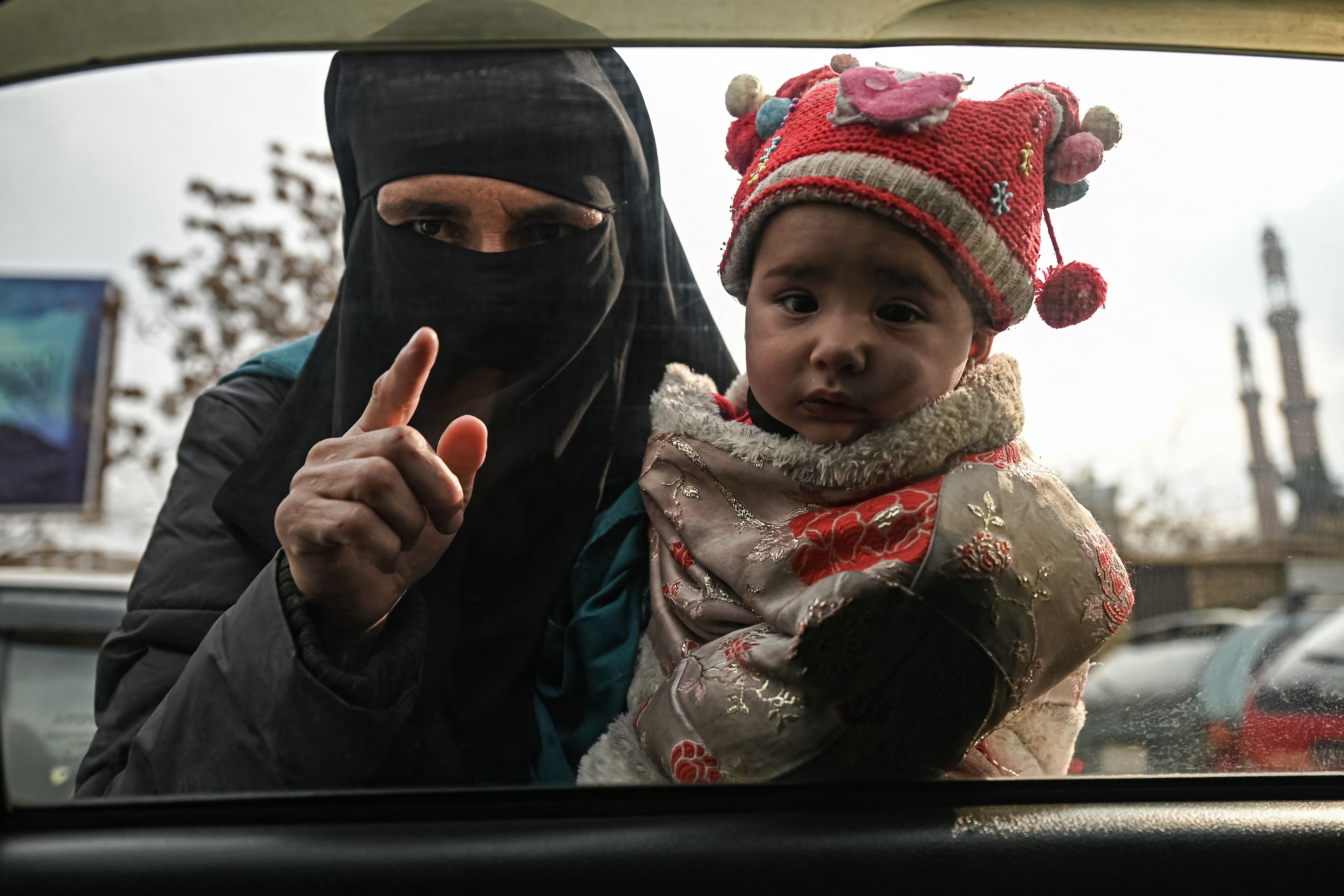 A woman carries a child as she begs from commuters in a car in Kabul