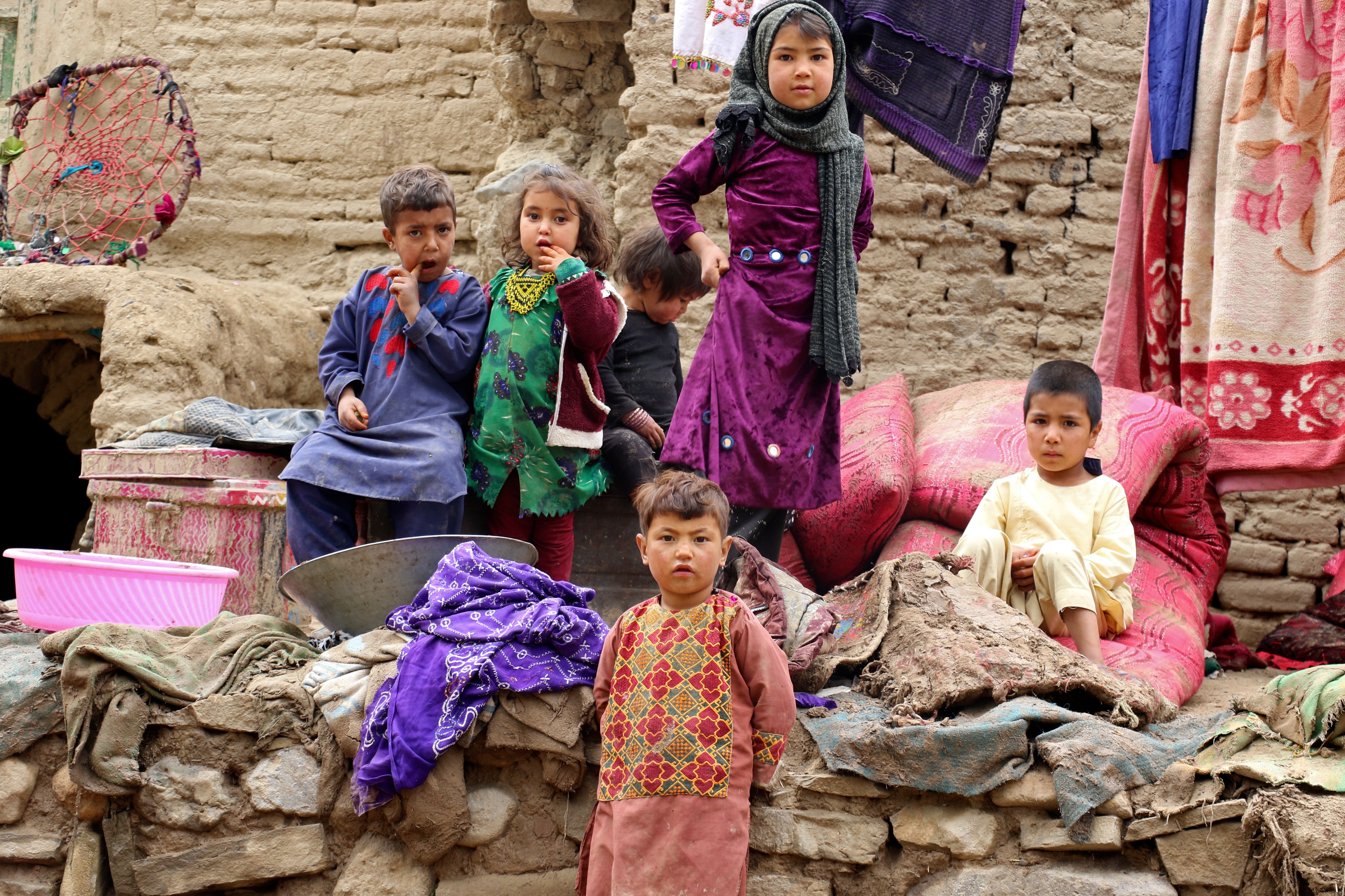 Children affected by a flash flood sit outside their damaged home in the Qadis district, Badghis province, in May 2022