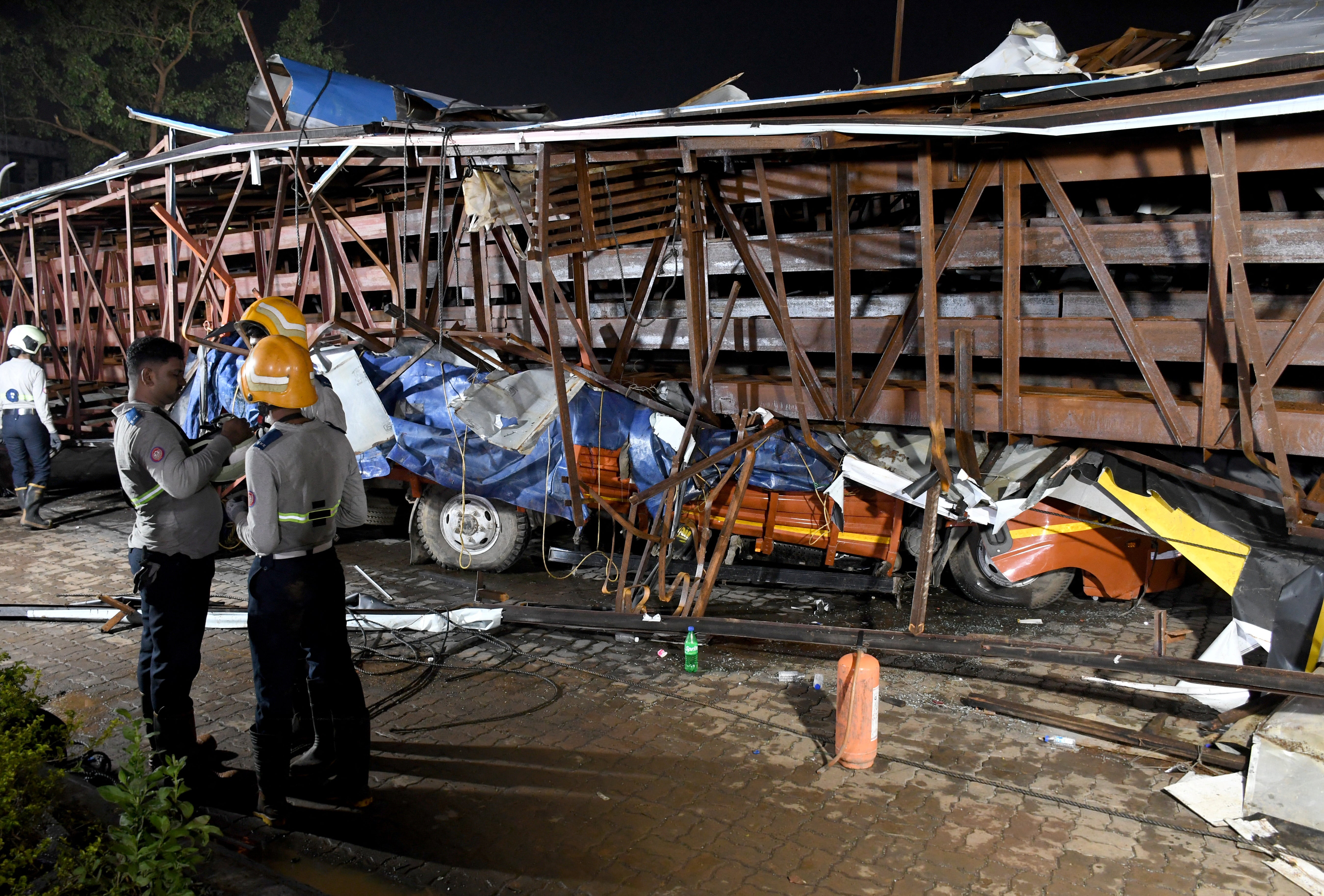 Firefighters stand next to the damaged vehicles trapped in the debris