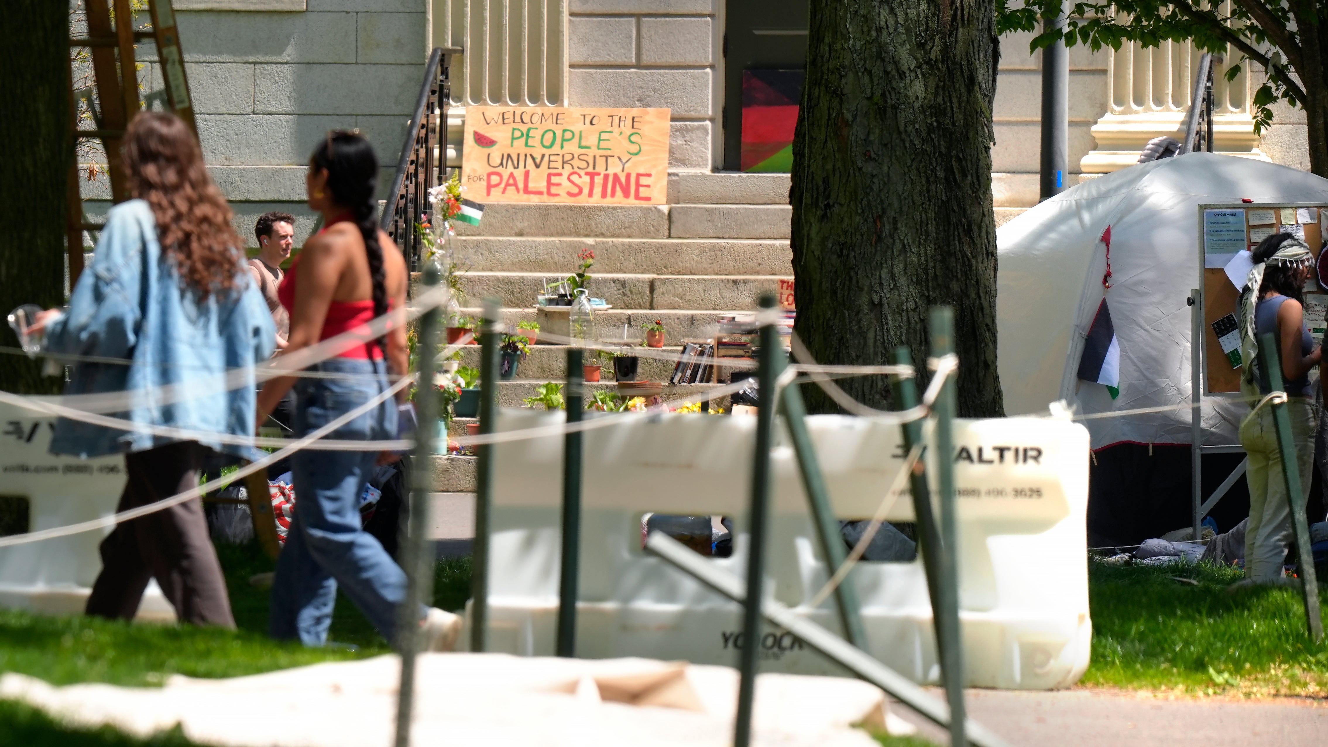 People walk past the remnants of an encampment of tents in Harvard Yard on the campus of Harvard University, Tuesday, May 14, 2024, in Cambridge, Mass