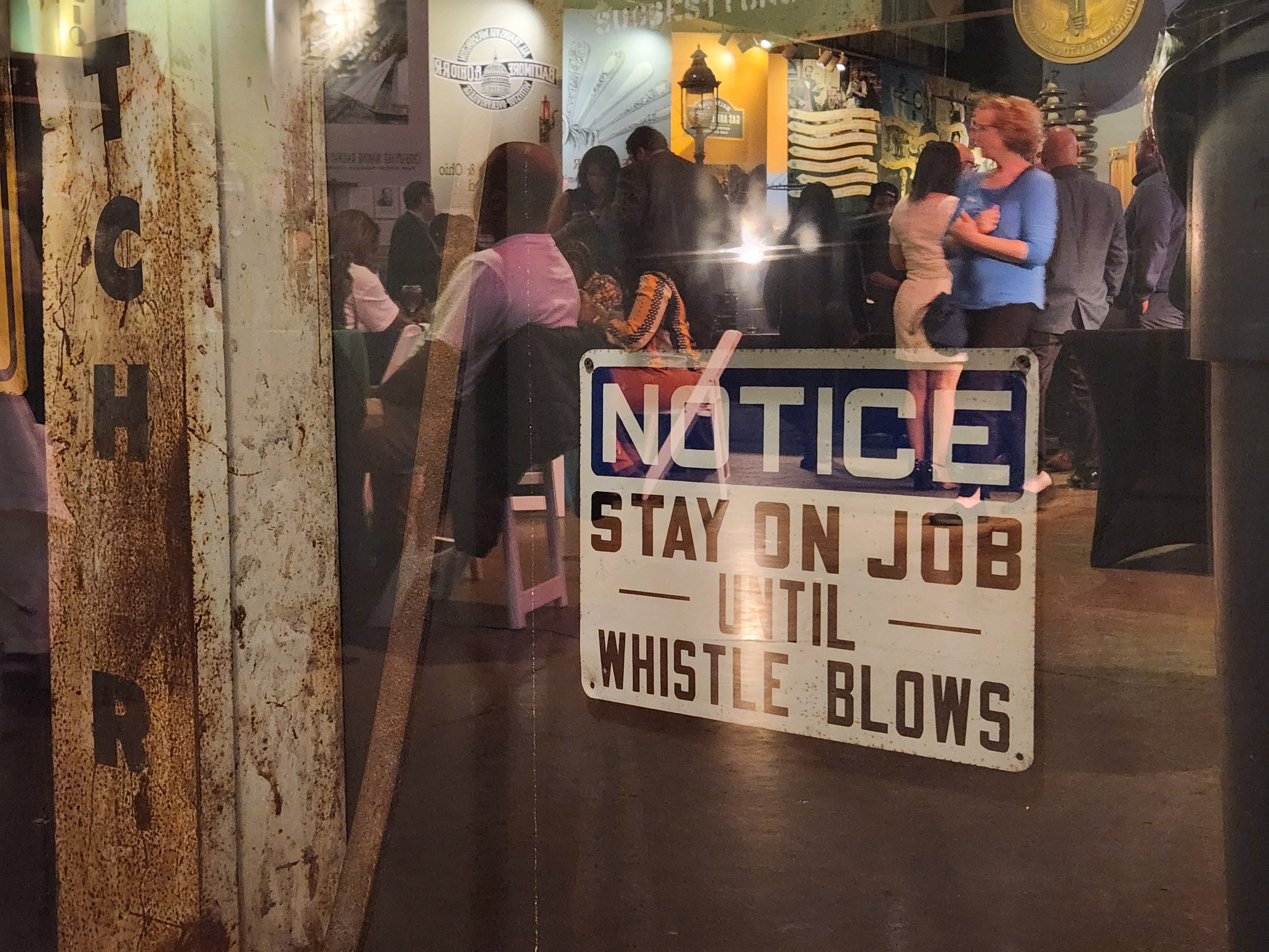 Attendees of David Trone’s election night watch event are reflected in the glass protecting an exhibit at the Baltimore Museum of Industry