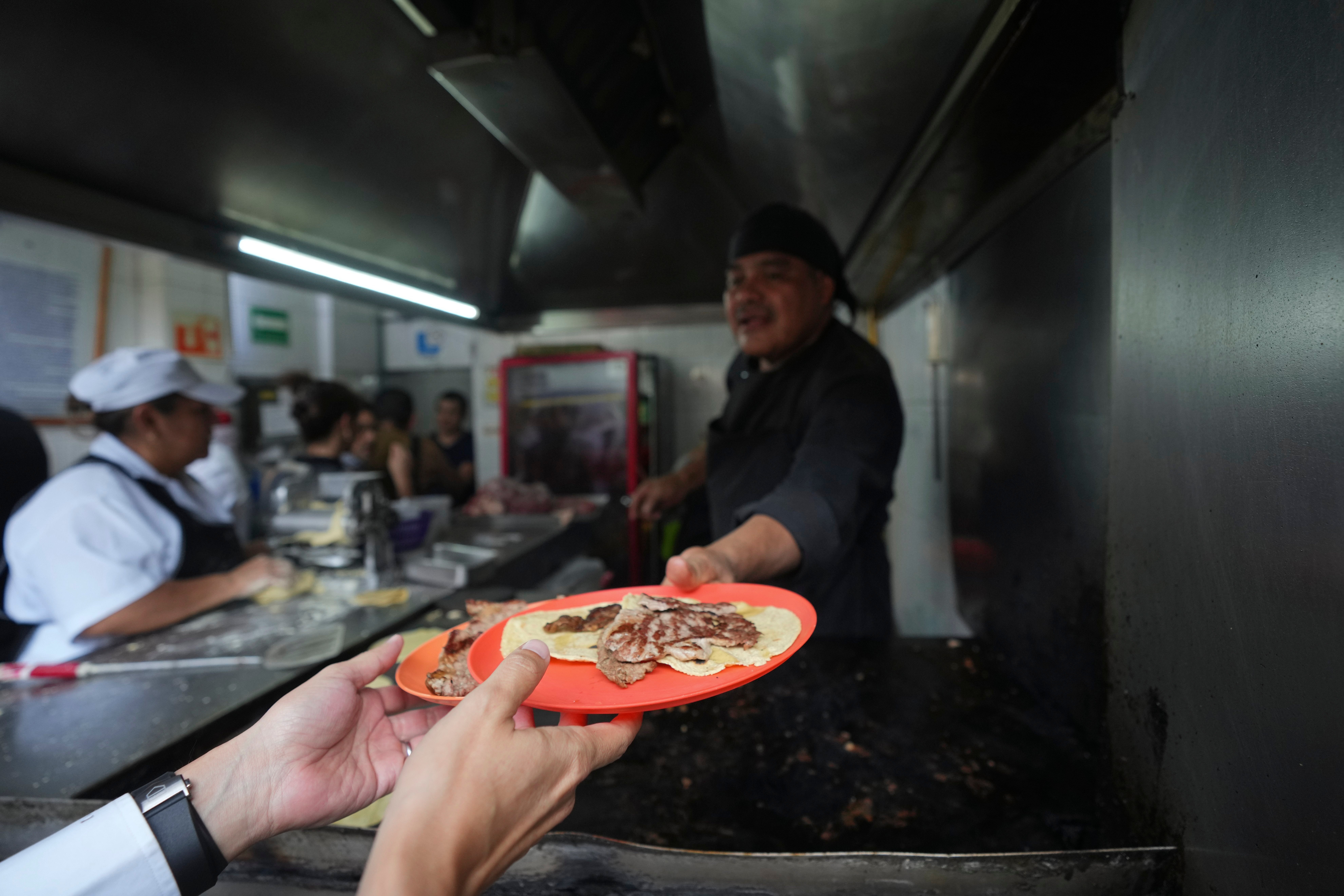 A worker hands a customer his order of tacos at the Tacos El Califa de León taco stand, in Mexico City