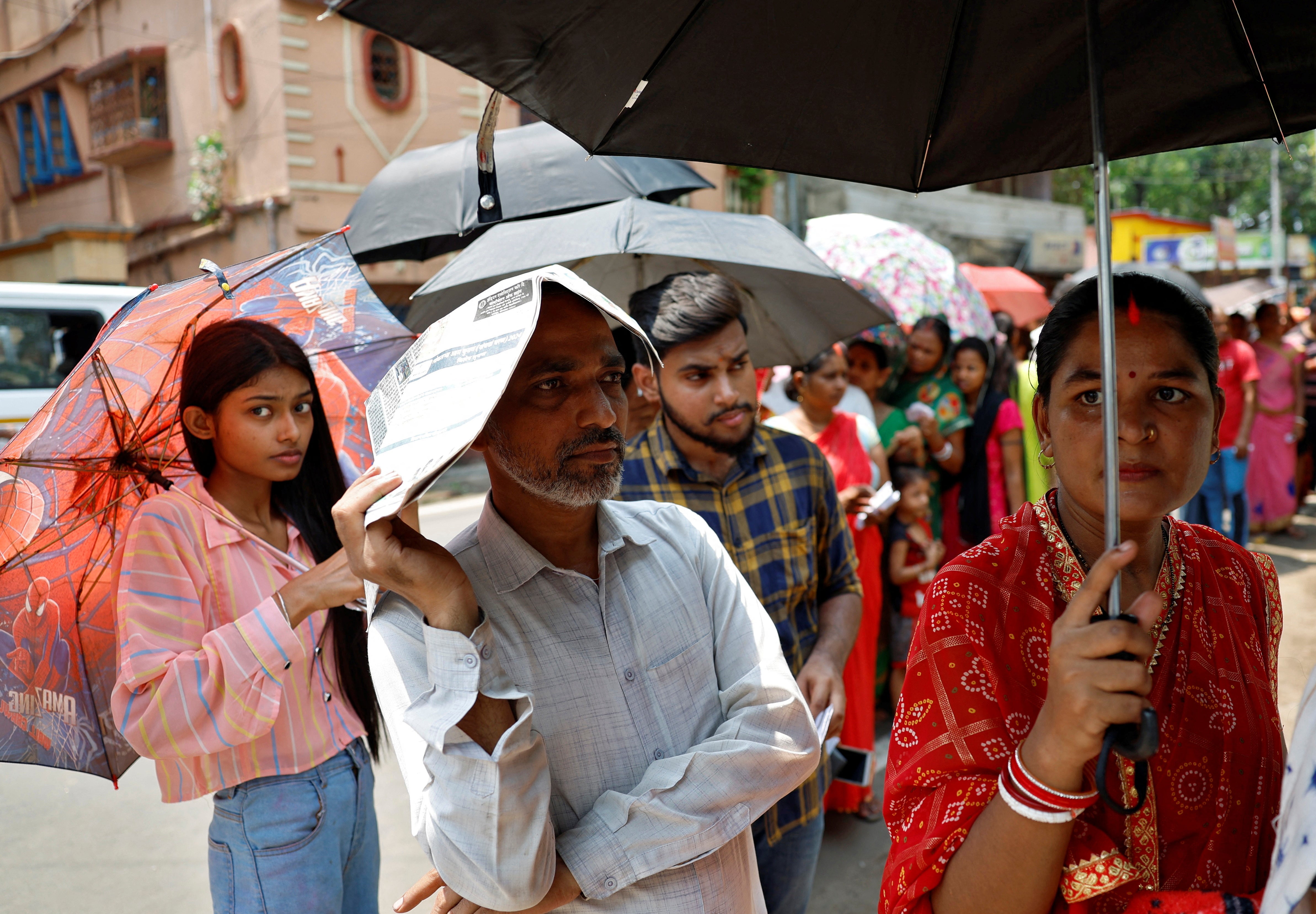 People use newspapers and umbrellas to protect themselves from the heat as they wait to vote outside a polling station