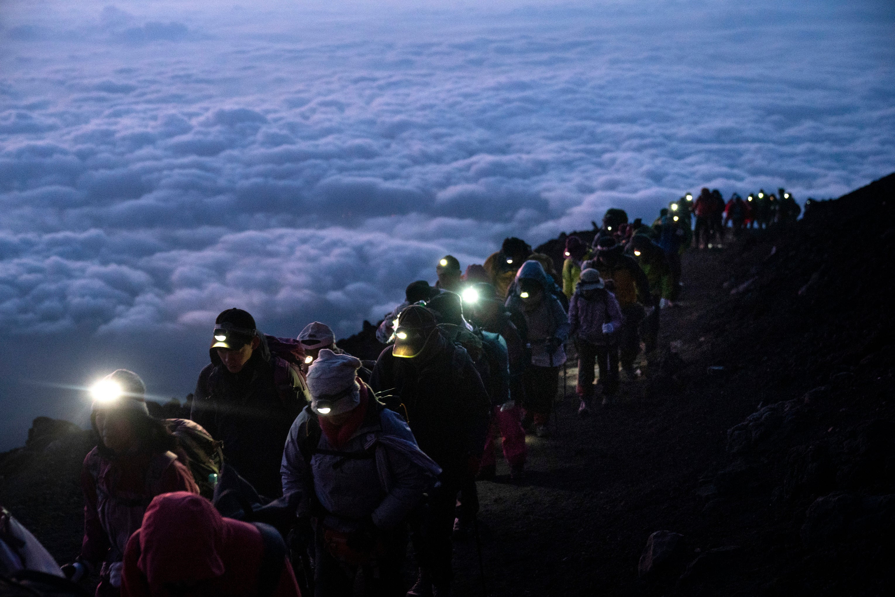 A group of hikers climb to the top of Mount Fuji just before sunrise as clouds hang below the summit Tuesday, Aug. 27, 2019, in Japan