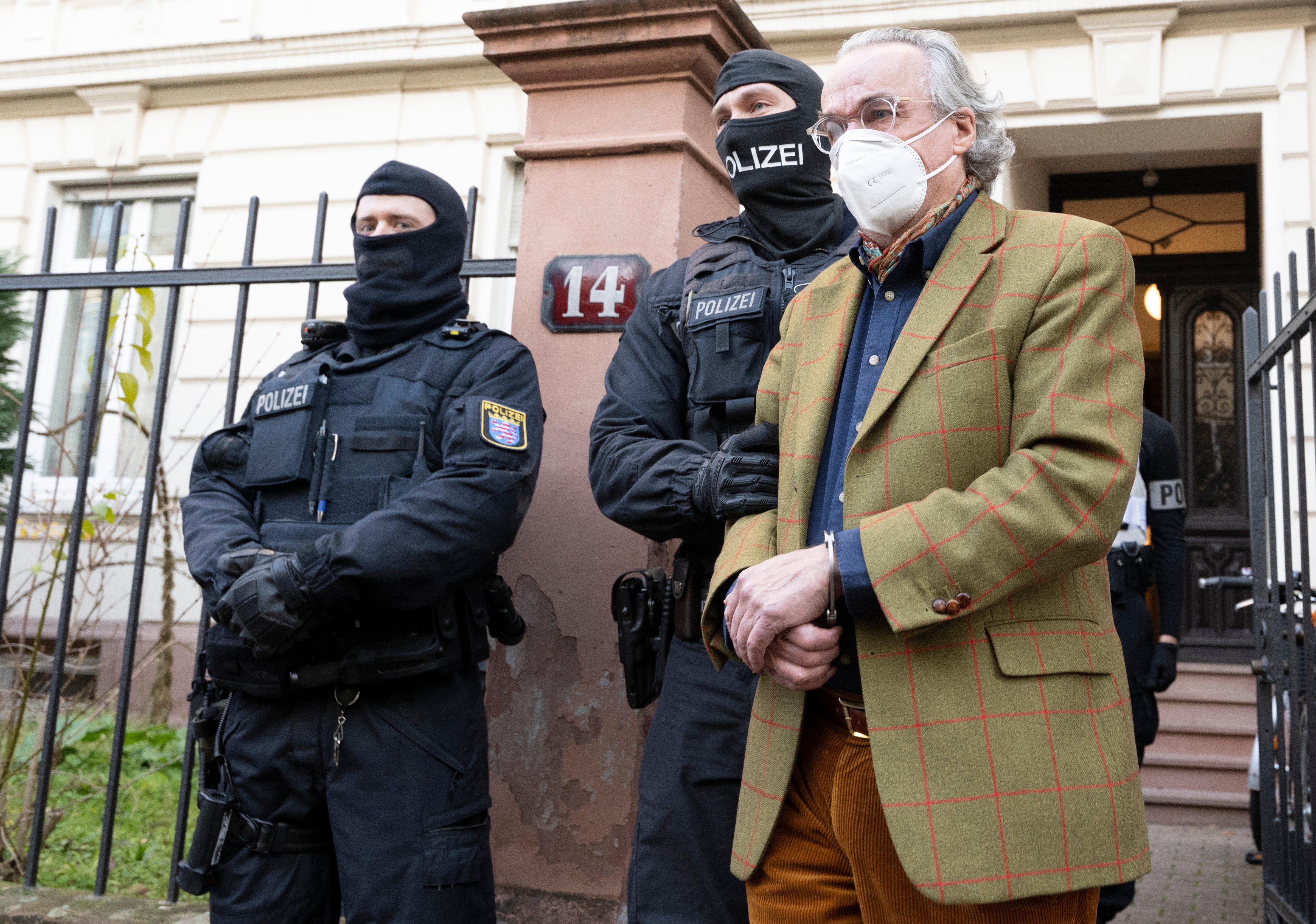 Masked police officers lead Heinrich XIII Prince Reuss, right, to a police vehicle