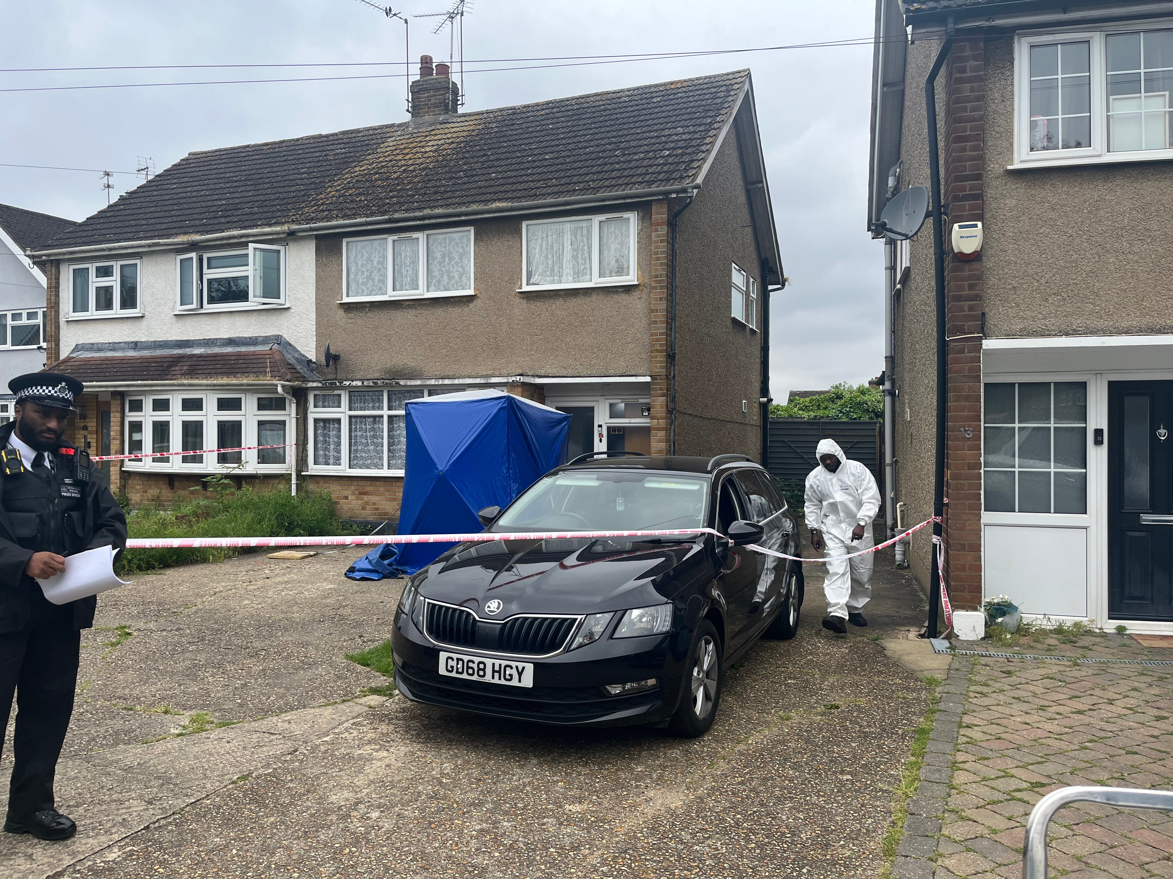 A black car parked on the driveway as a police officer guards the scene