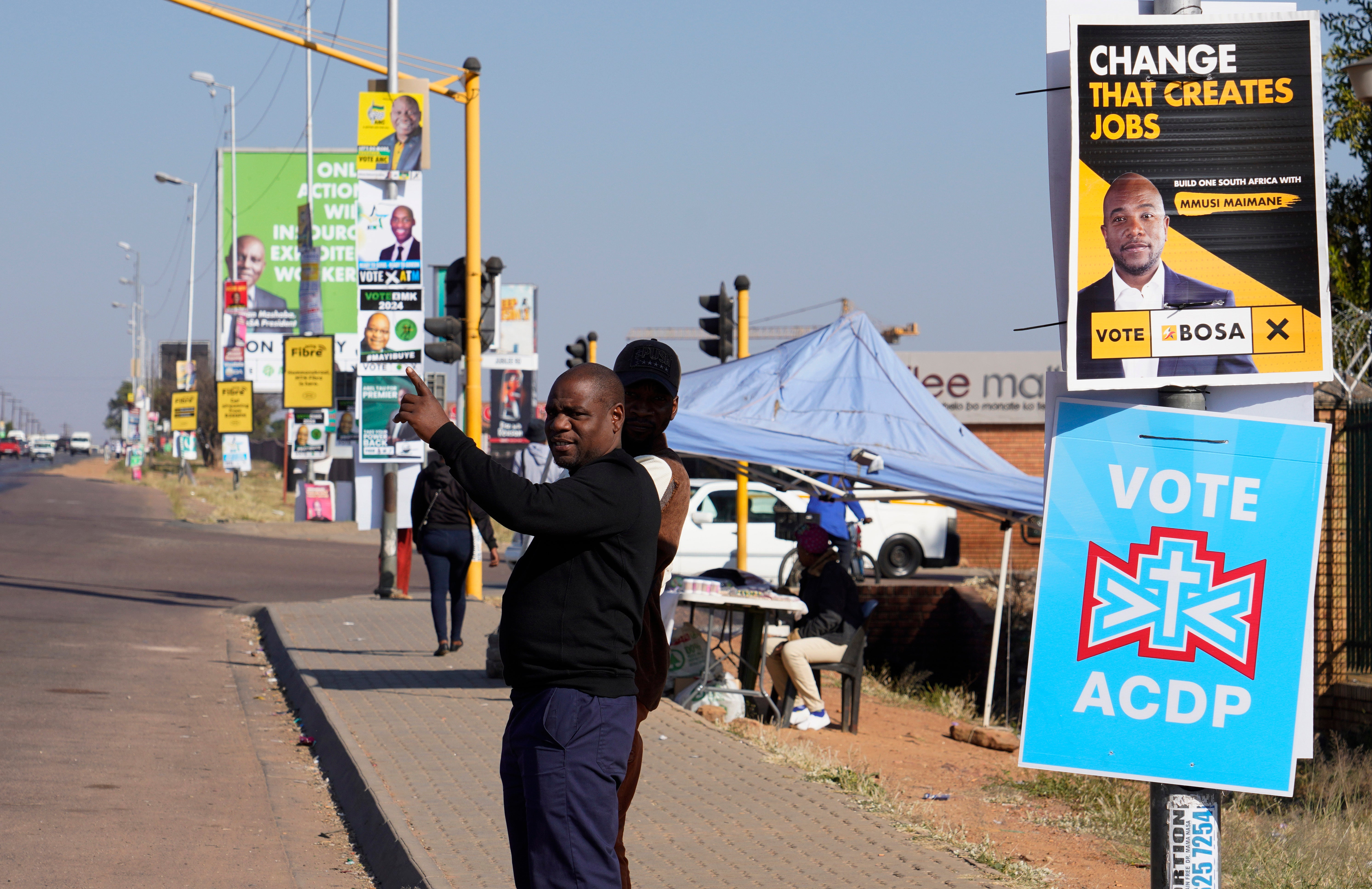 A man waits for a taxi along a street lined with election posters in the Hammanskraal township, Pretoria