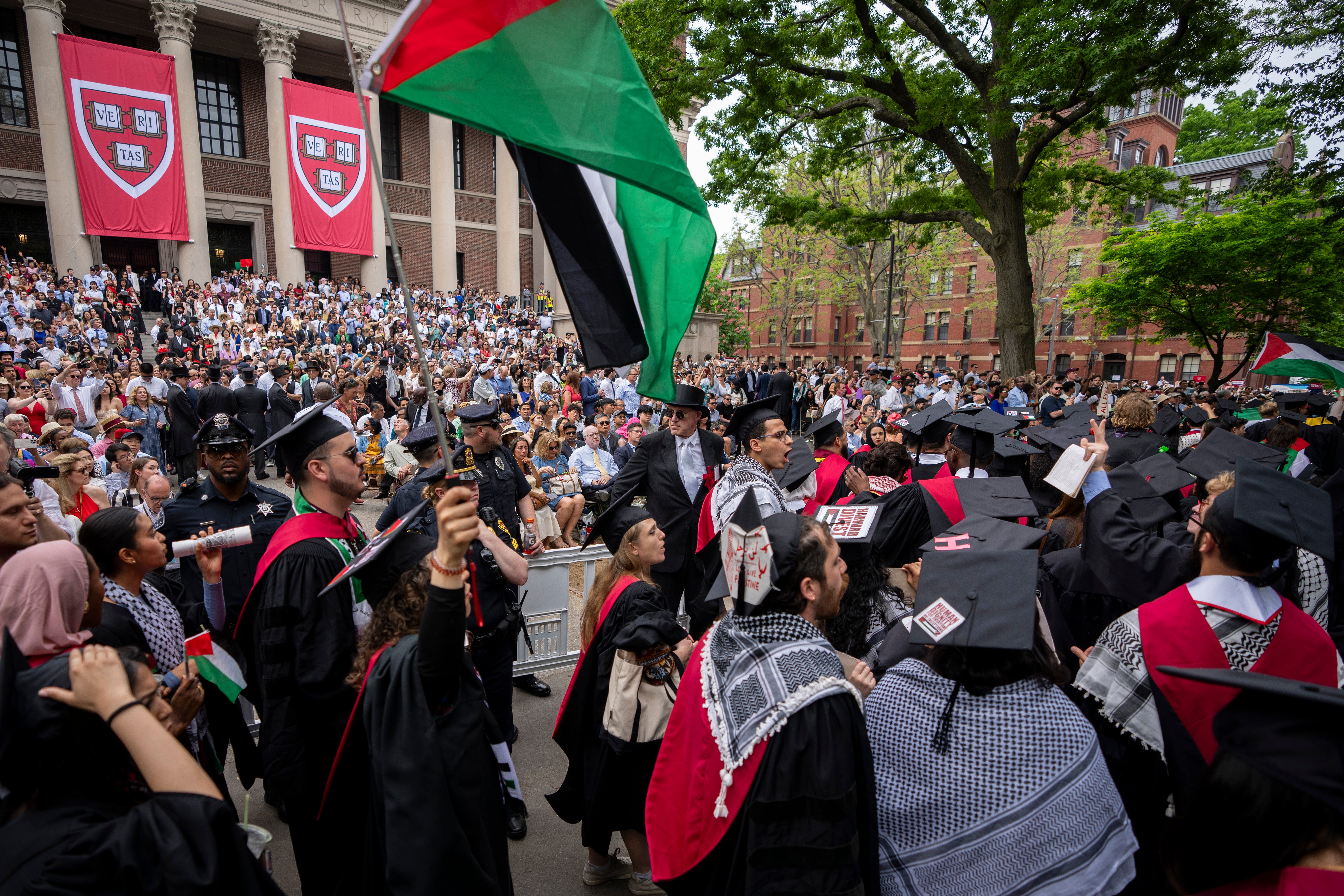 Graduating students hold Palestinian flags and chant as they walk out in protest over the 13 students who have been barred from graduating due to protest activities, during commencement in Harvard Yard