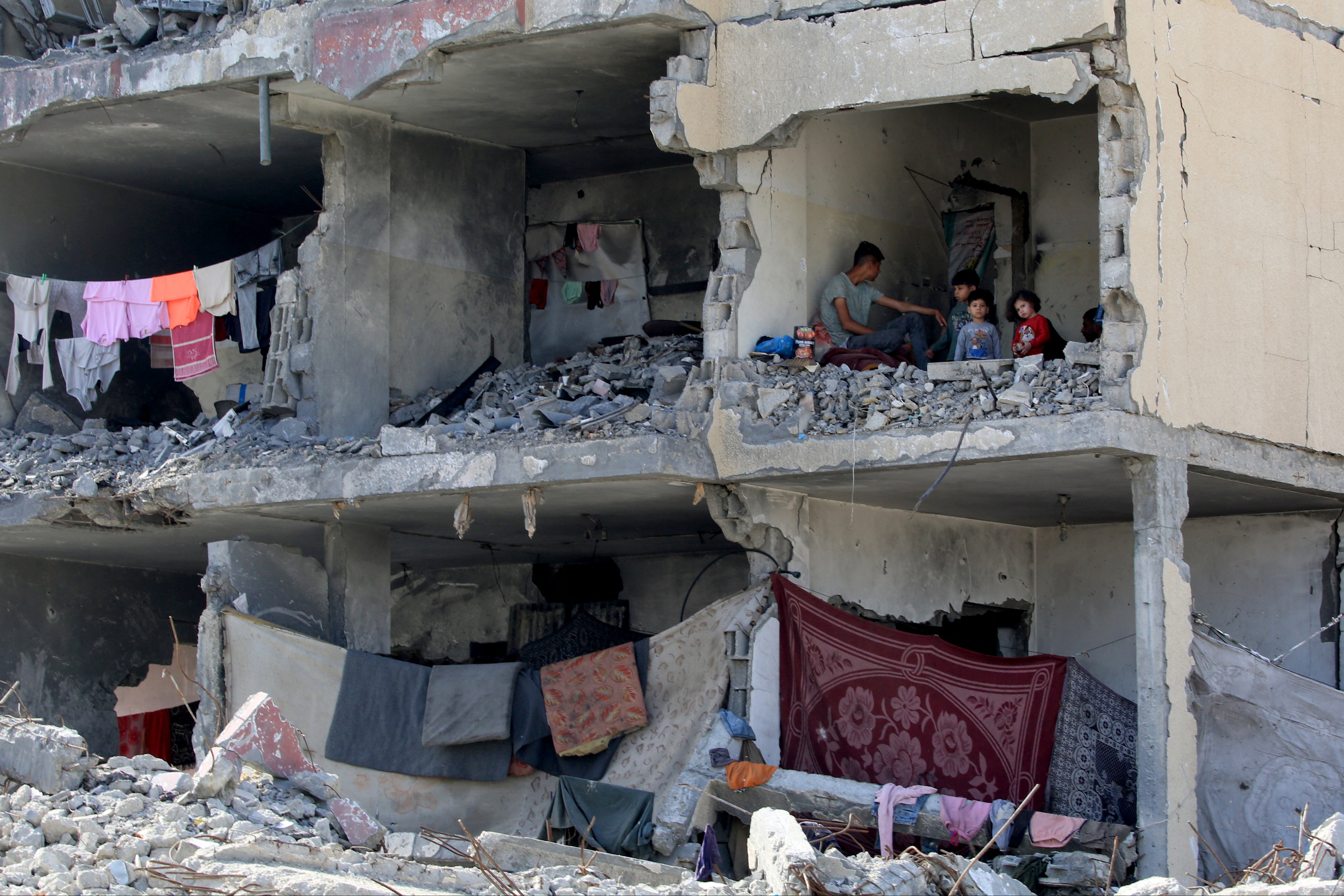 A Palestinian man and his children sit in a destroyed room following the targeting or a residential building by an Israeli airstrike in Rafah