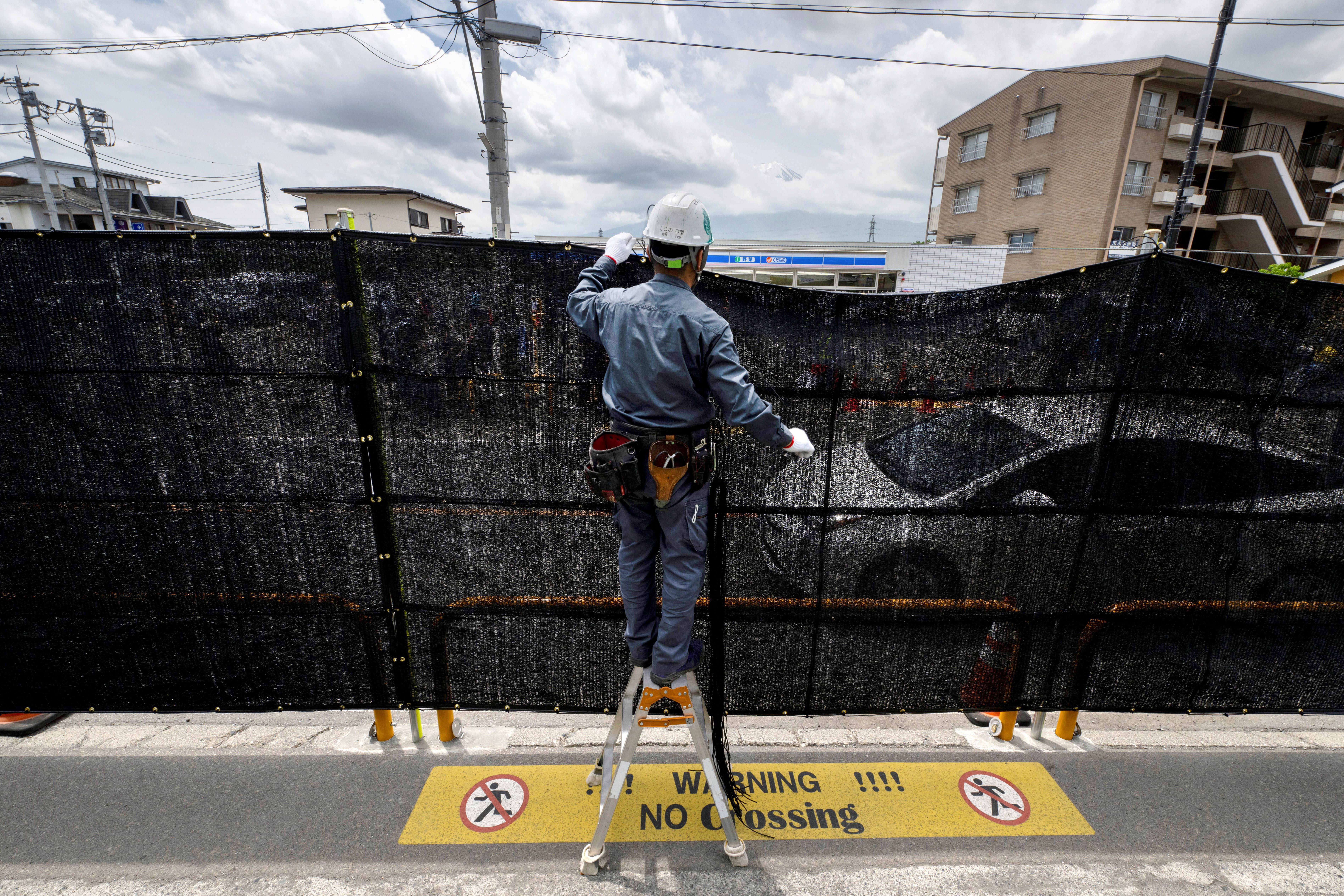 A worker installs a barrier to block the sight of Japan’s Mount Fuji emerging from behind a convenience store