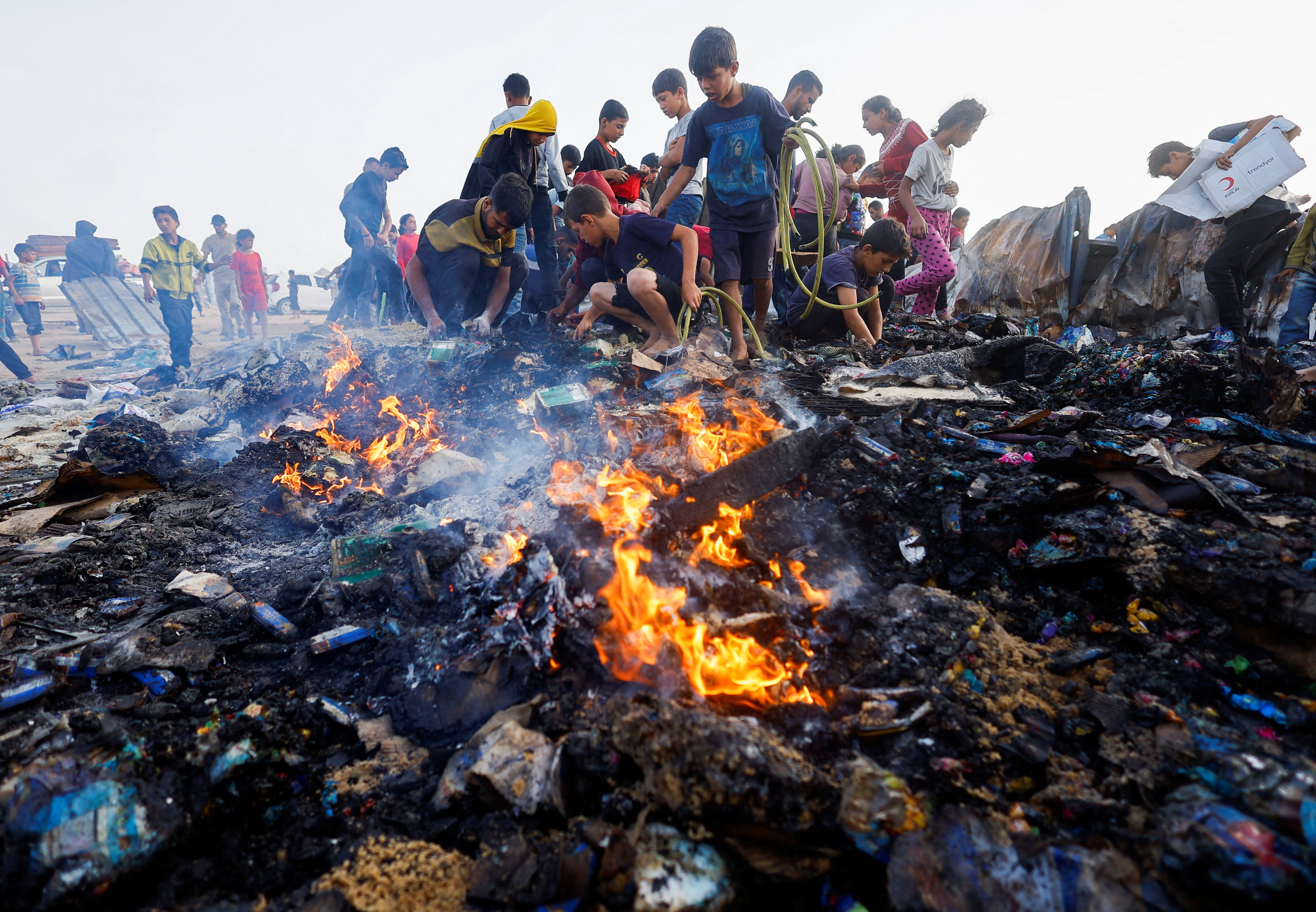 Palestinians search for food among burnt debris in the aftermath of an Israeli strike on an area designated for displaced people, in Rafah in the southern Gaza Strip, 27 May 2024