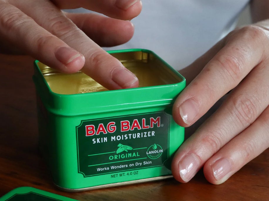 A hand dips into a tin of Vermont’s Original Bag Balm skin moisturizer