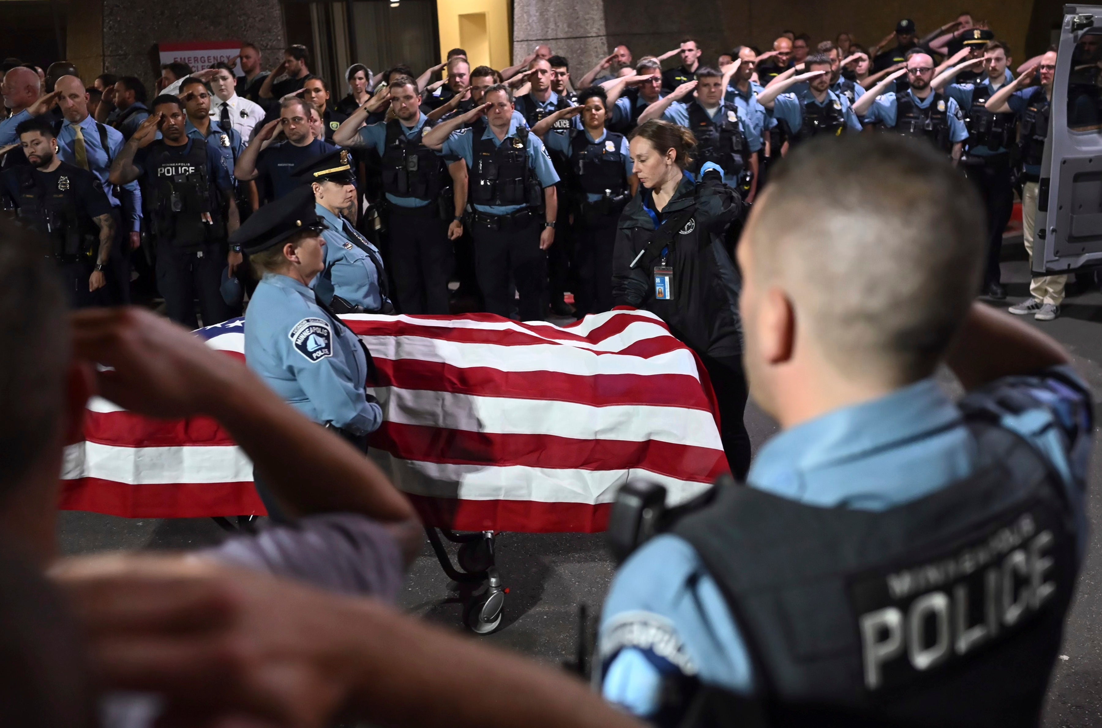 Law enforcement officers salute the flag-draped remains of Jamal Mitchell as he is escorted to a waiting medical examiner's vehicle outside Hennepin County Medical Center