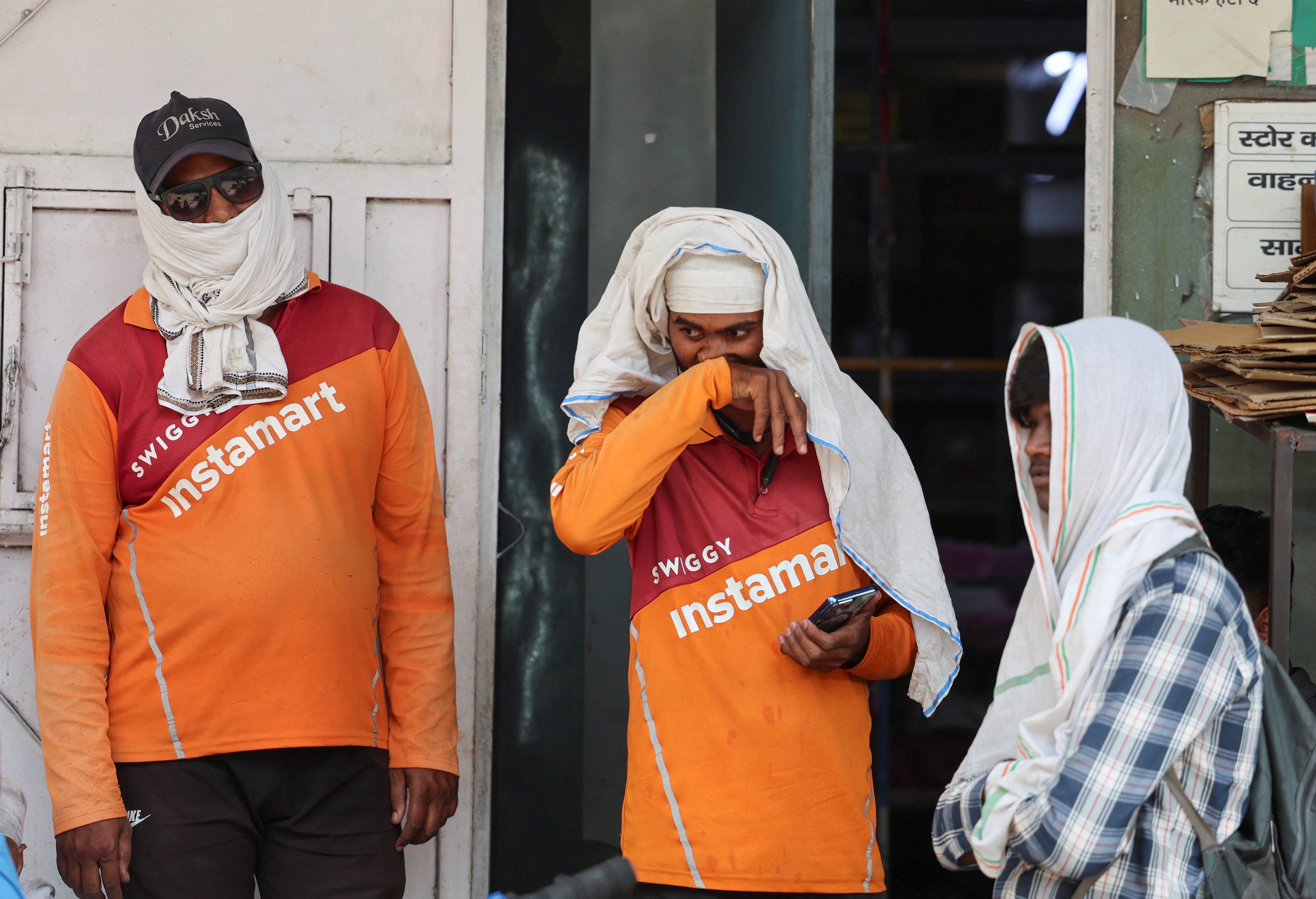 A delivery partner with the Indian online delivery company Swiggy wipes sweat off his face as he waits outside with other delivery partners at one of Swiggy’s Instamart dark stores on a hot summer day, during a heatwave in New Delhi