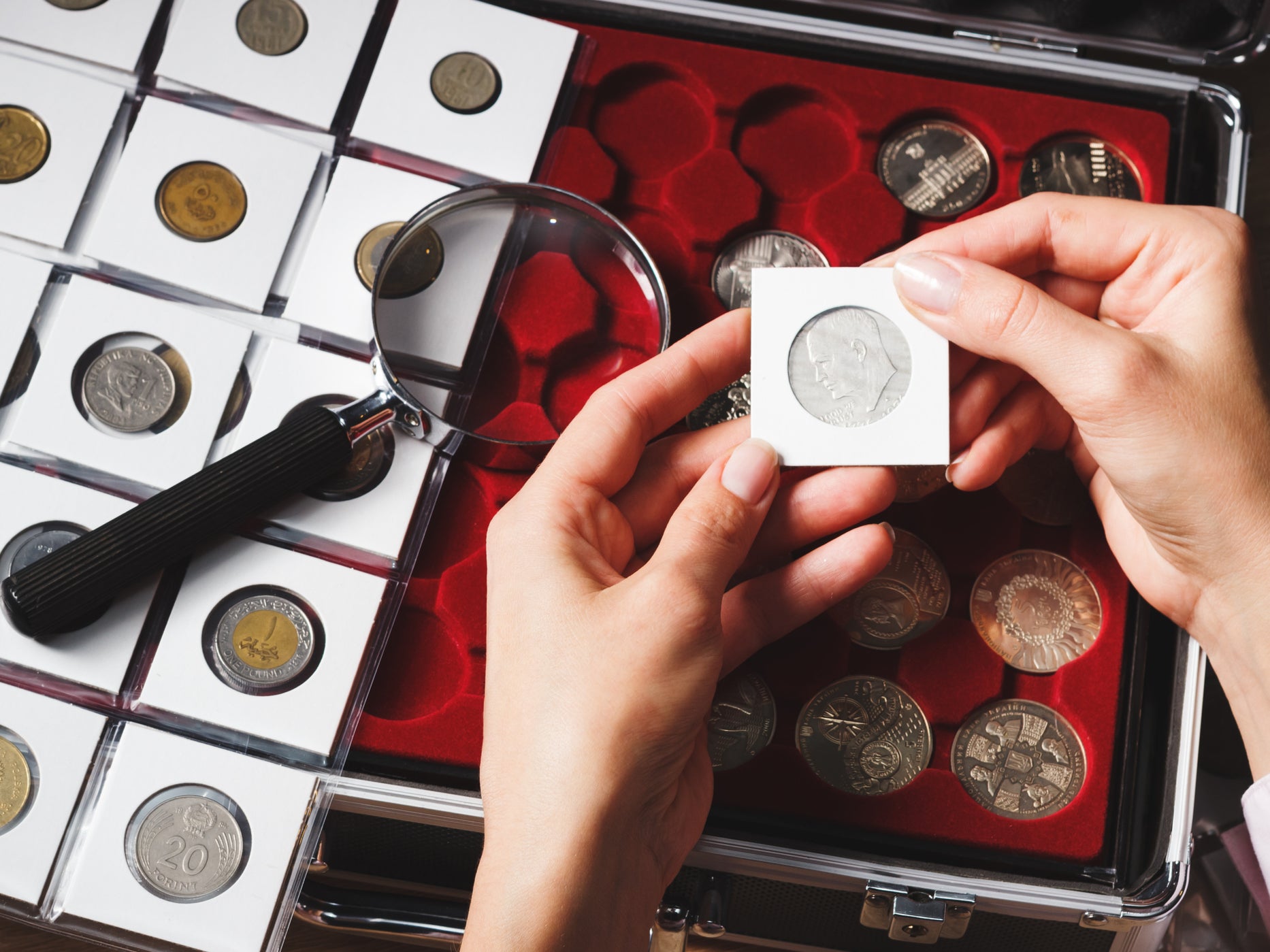 A box with collectible coins in cells and a hand holding a coin. According to a May YouGov poll of nearly 3,000 American adults, over 80 percent reported they would stop to pick up coins on the street, with the habit being common among older adults.