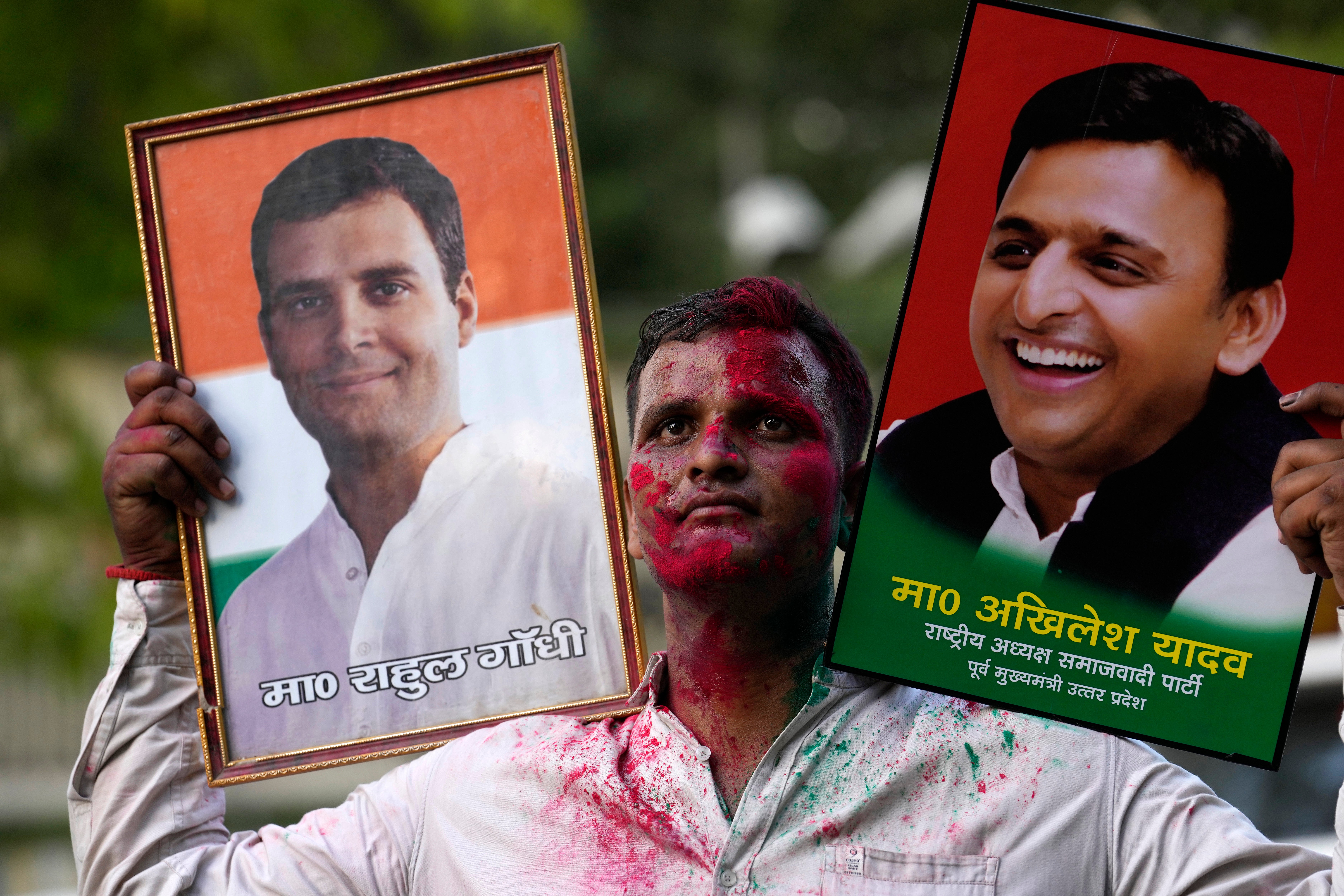 A Samajwadi Party supporter carries portraits of party leader Akhilesh Yadav, right, and Congress Party leader, Rahul Gandhi, as he celebrates his party’s lead during the counting of votes in Lucknow