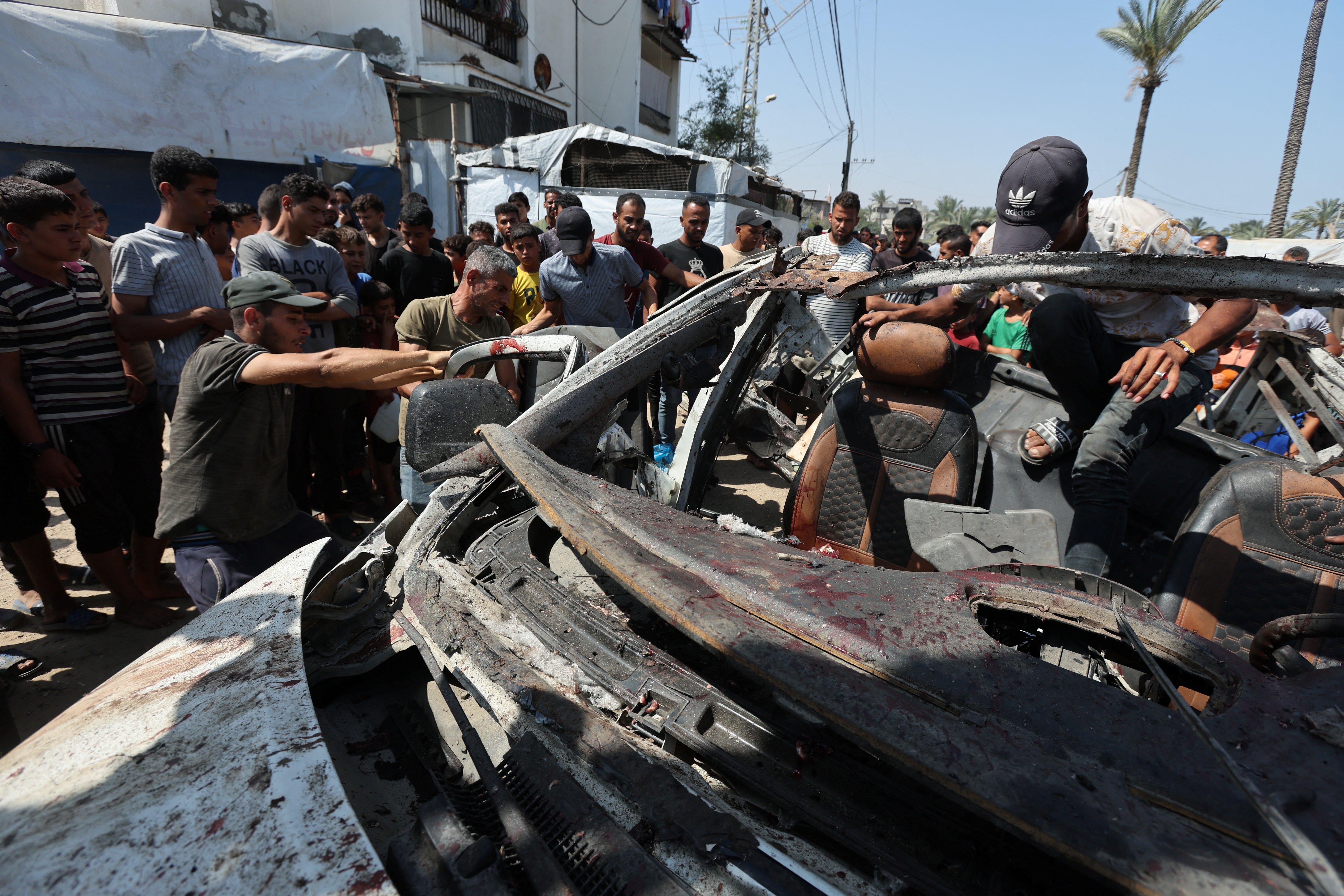 Palestinians inspect a vehicle hit in an Israeli strike in Deir Al-Balah in the central Gaza Strip