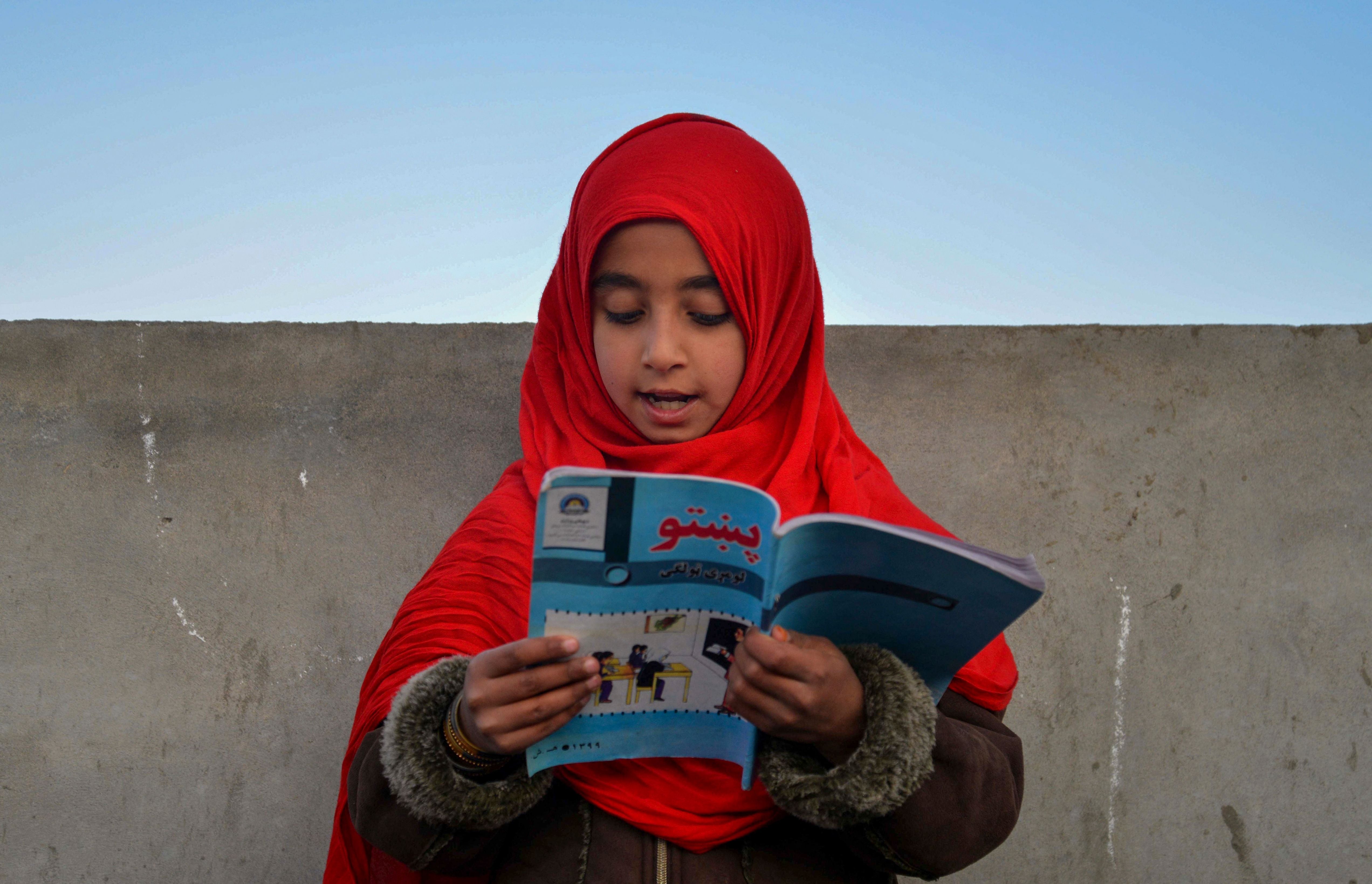 An Afghan girl reads a book in an open classroom in Kandahar province