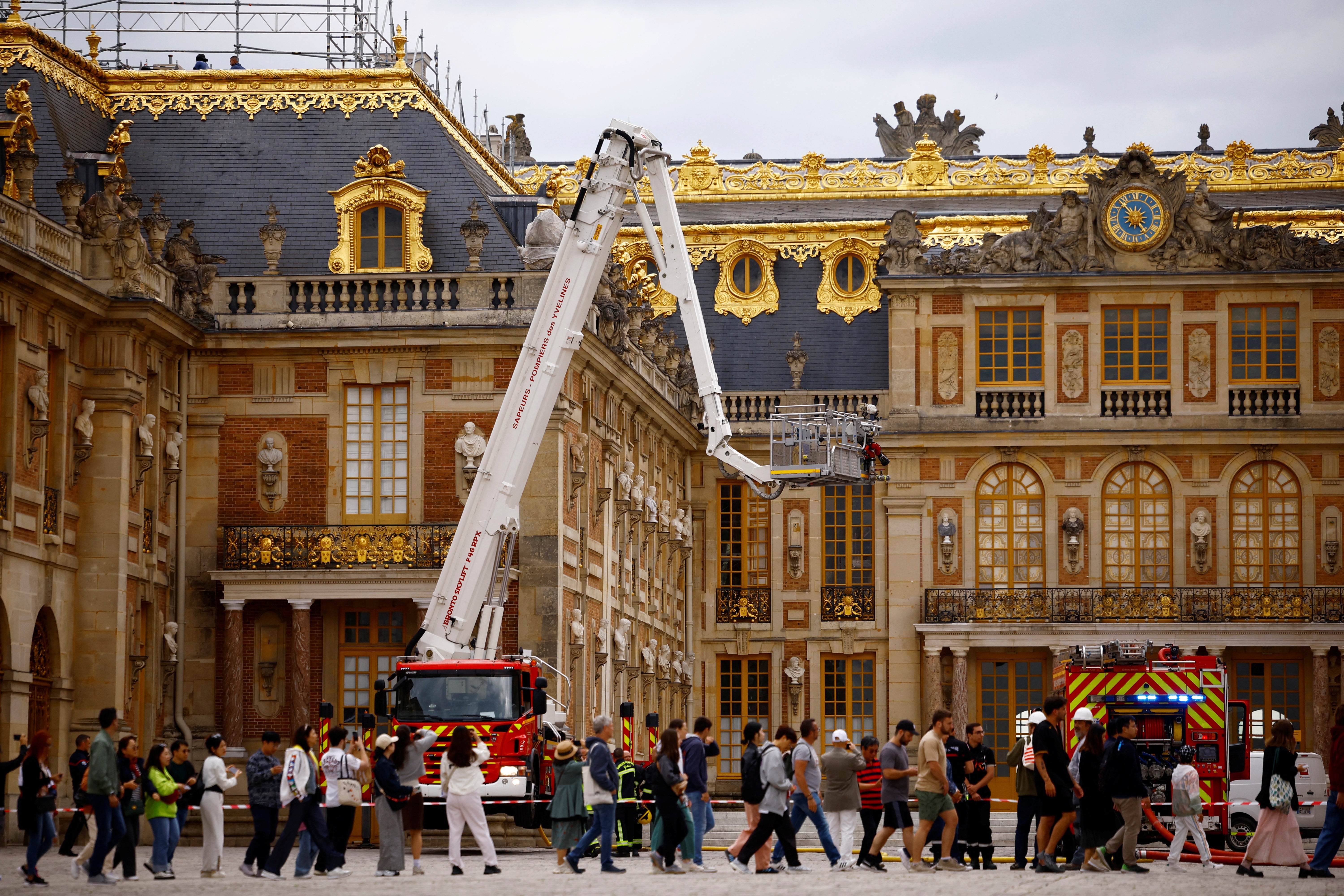 Visitors walk past as French firefighters work after a fire broke out at the Chateau de Versailles