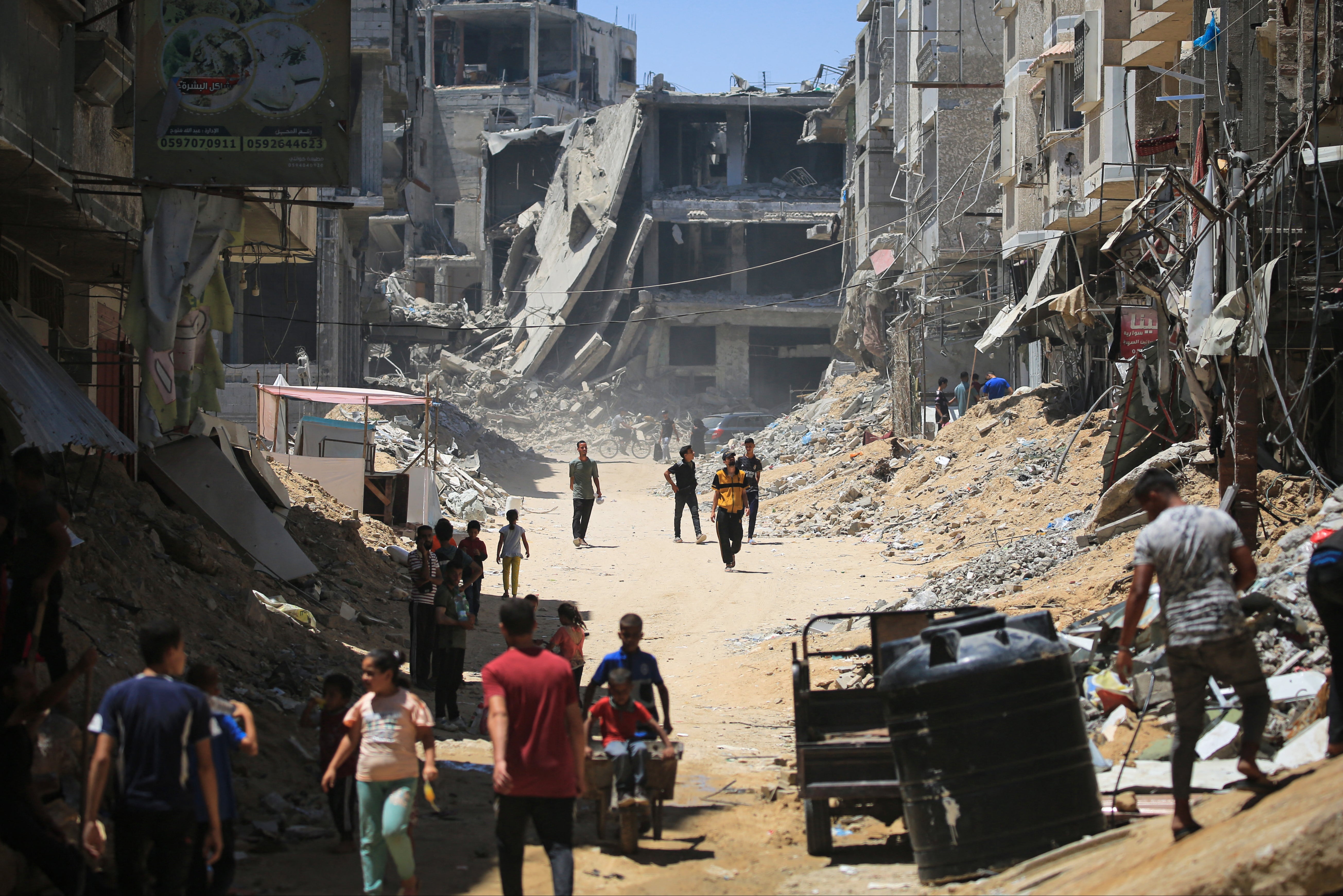 Palestinian citizens walk past buildings destroyed in the Israeli bombardment of Khan Younis, in the southern Gaza Strip