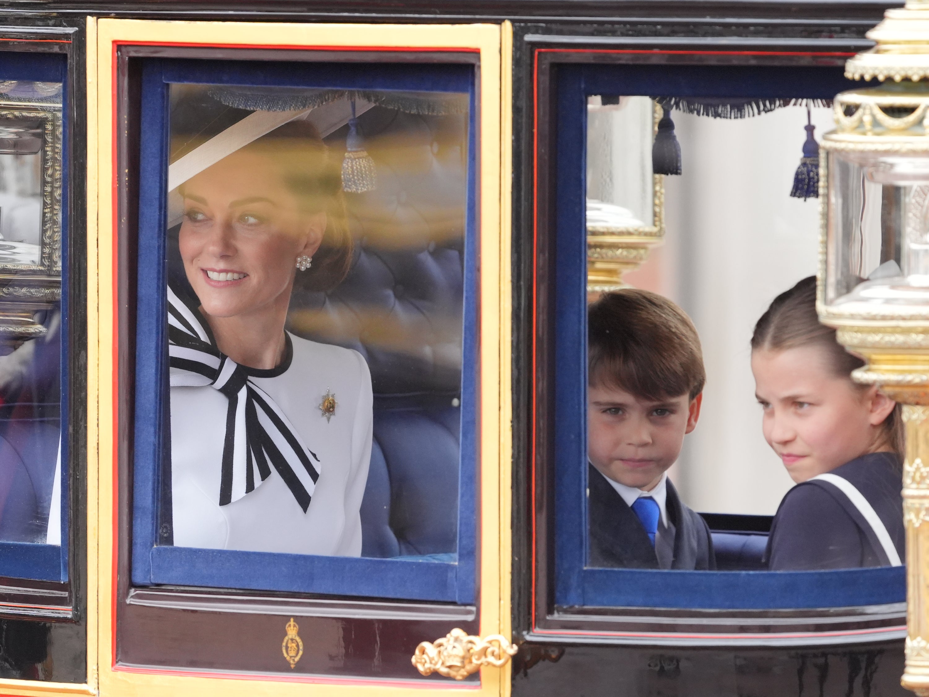 Prince Louis and Princess Charlotte look out at the crowds while their mother smiles and waves