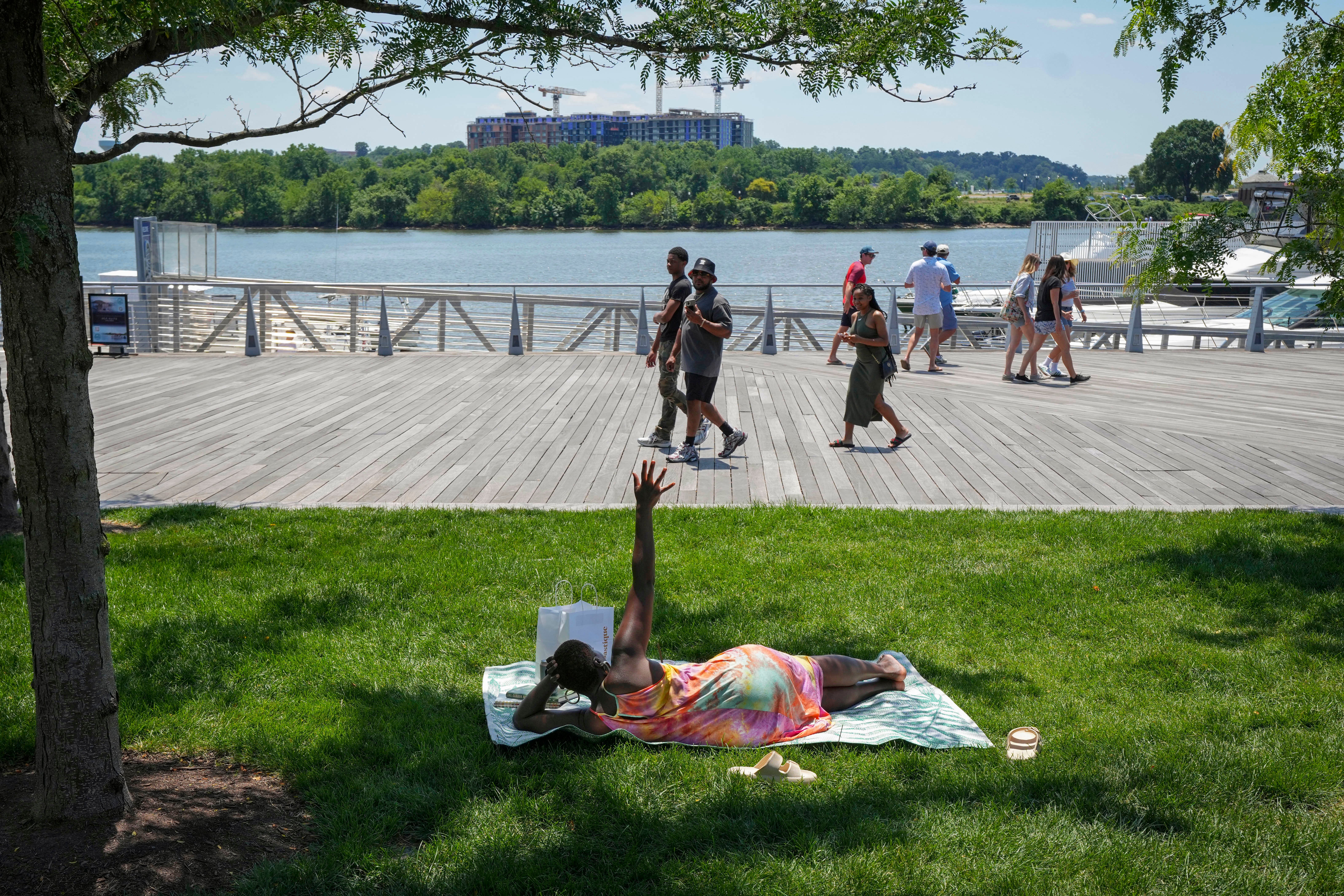 Forecasters say more than 135 million Americans will face temperatures above 90 degrees for most of the week. A woman stretches up her hand while lying in a patch of shade with a book at Yards Park near Washington, DC