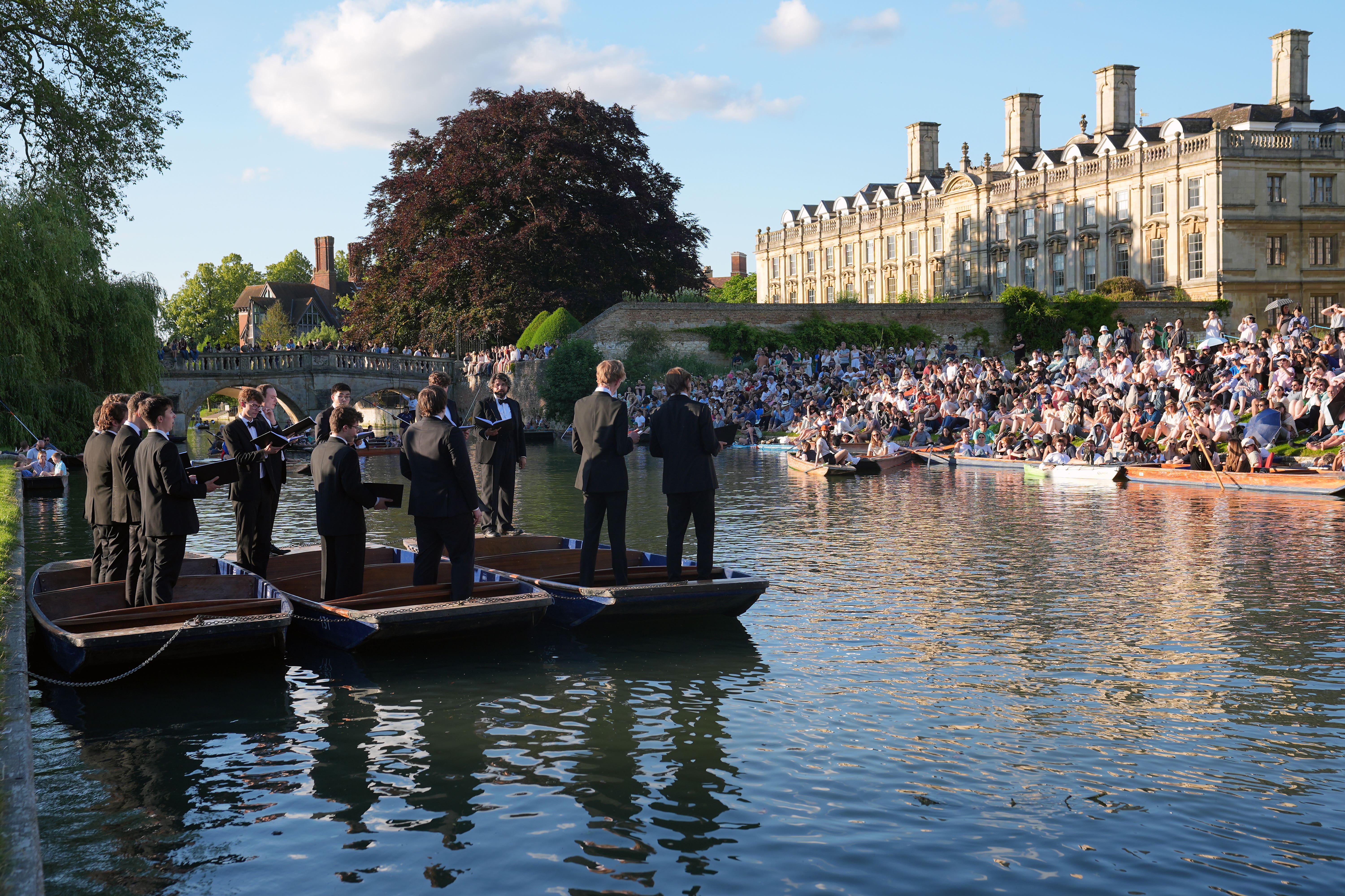 People sit on the banks of the River Cam and lawns of King’s College in Cambridge, as they listen to The King’s Men perform (Joe Giddens/PA)